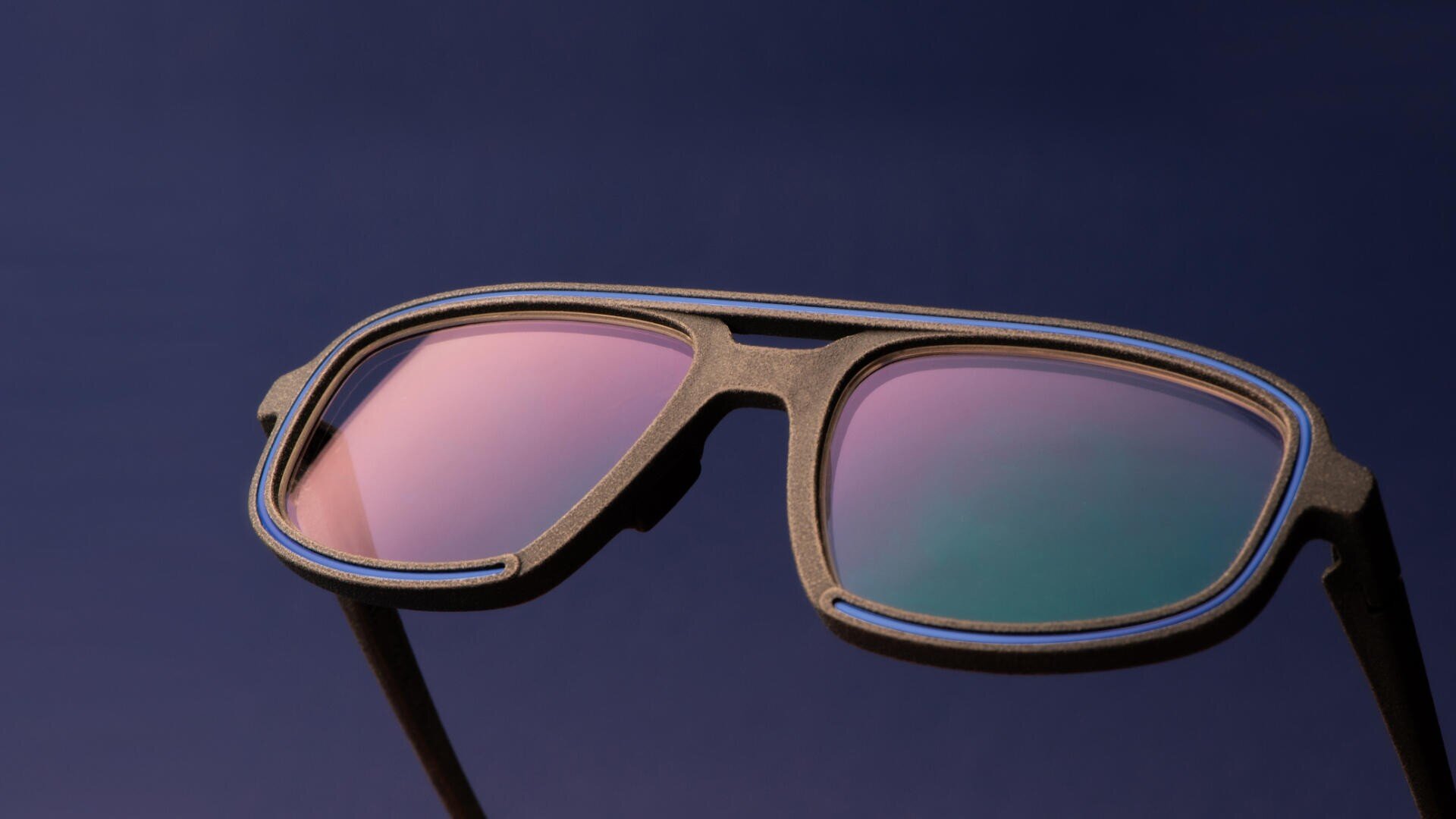 Close-up of black sunglasses with pink and green reflective lenses, set against a dark blue background.