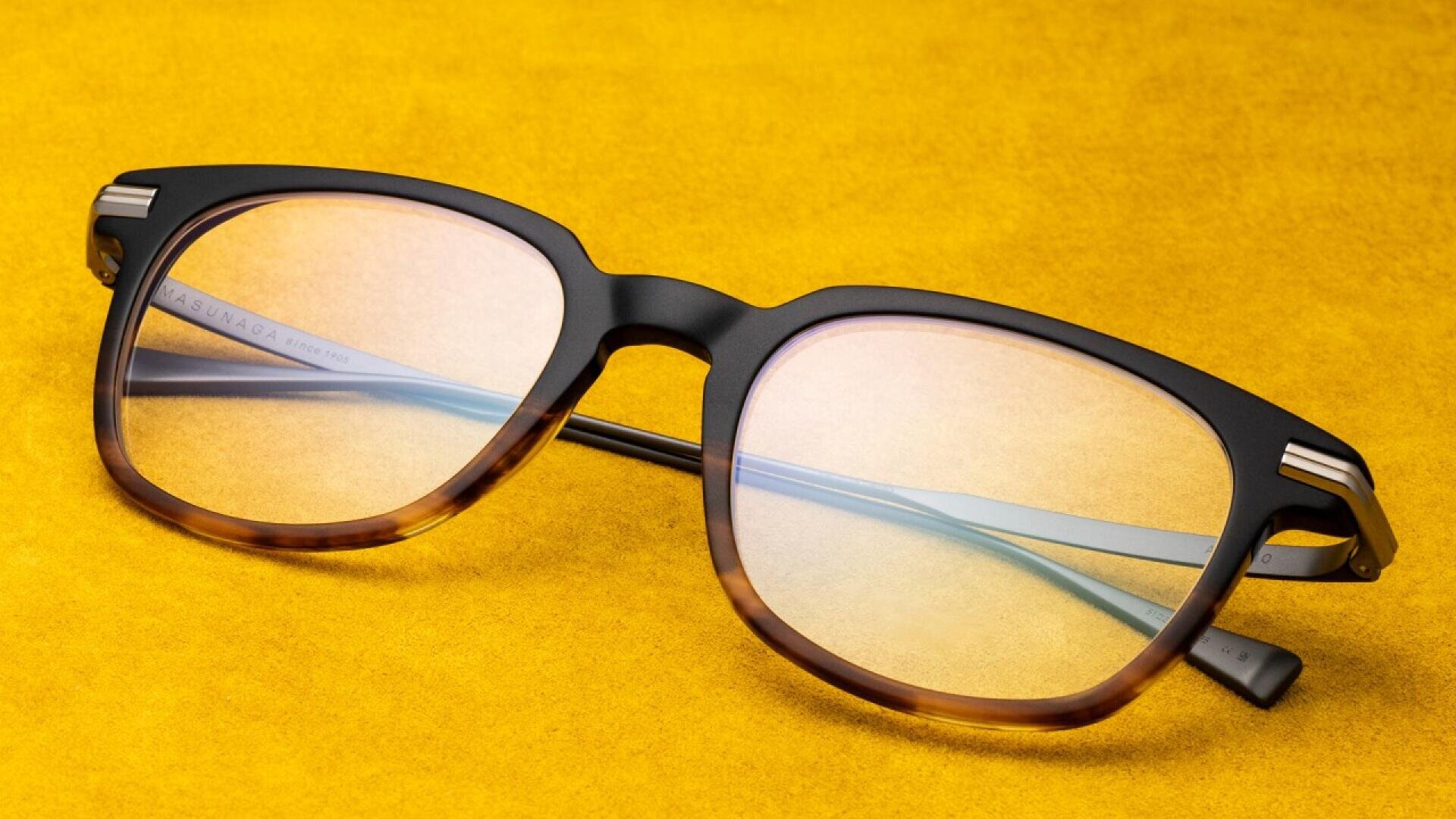 A pair of stylish eyeglasses with brown tortoiseshell frames and clear lenses rests on a bright yellow surface.