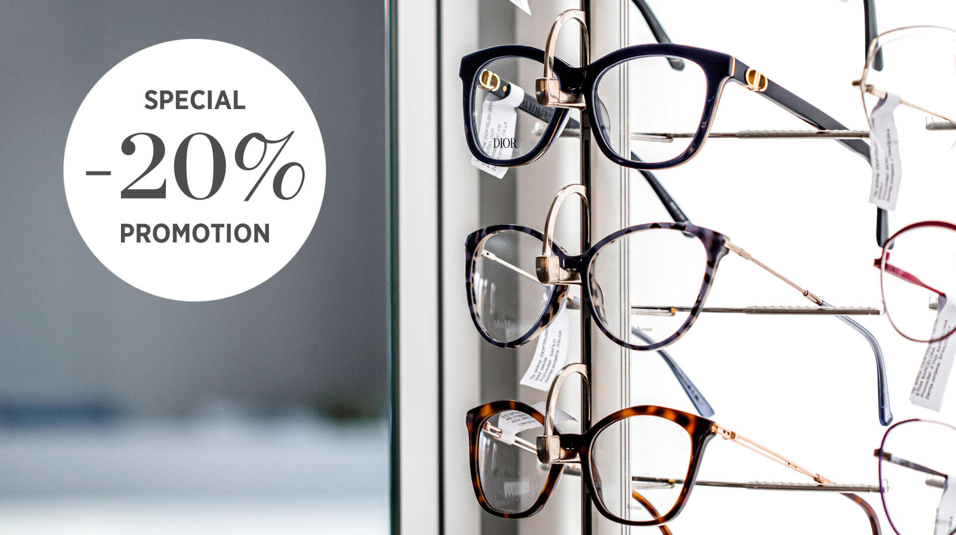 Eine Auslage mit Brillen auf einem Gestell neben einem runden Schild mit der Aufschrift SPECIAL -20% PROMOTION (Sonderangebot). Der Hintergrund ist leicht verschwommen und hebt die Brille und das Werbeangebot hervor.