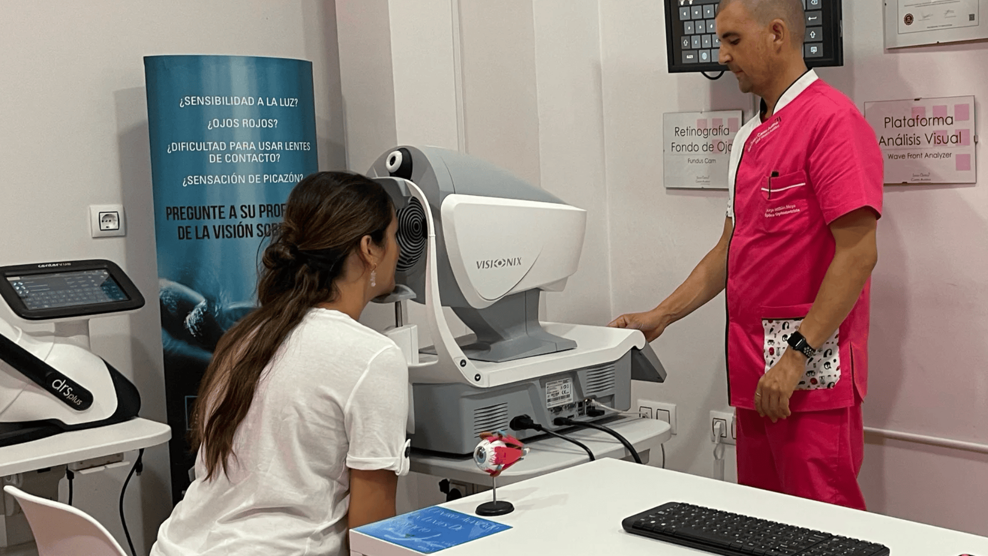Eine Frau sitzt an einem Augenuntersuchungsgerät, während eine medizinische Fachkraft in rosa OP-Kleidung neben ihr steht und bereit ist, in einer modernen Klinik einen Sehtest durchzuführen.