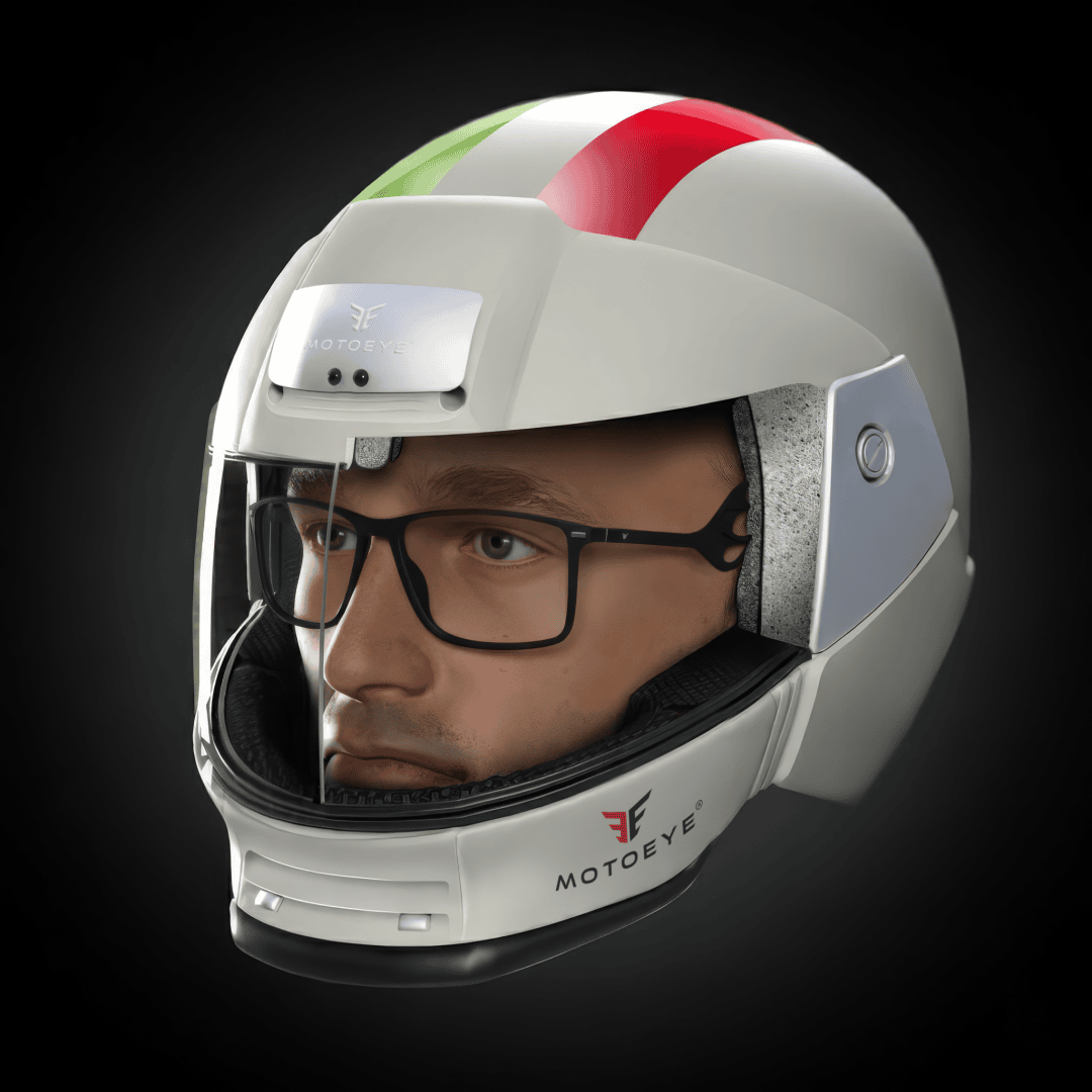 A man wearing goggles and a white motorcycle helmet with red and green stripes, a clear visor and a MOTOEYE logo on his chin can be seen against a dark background.
