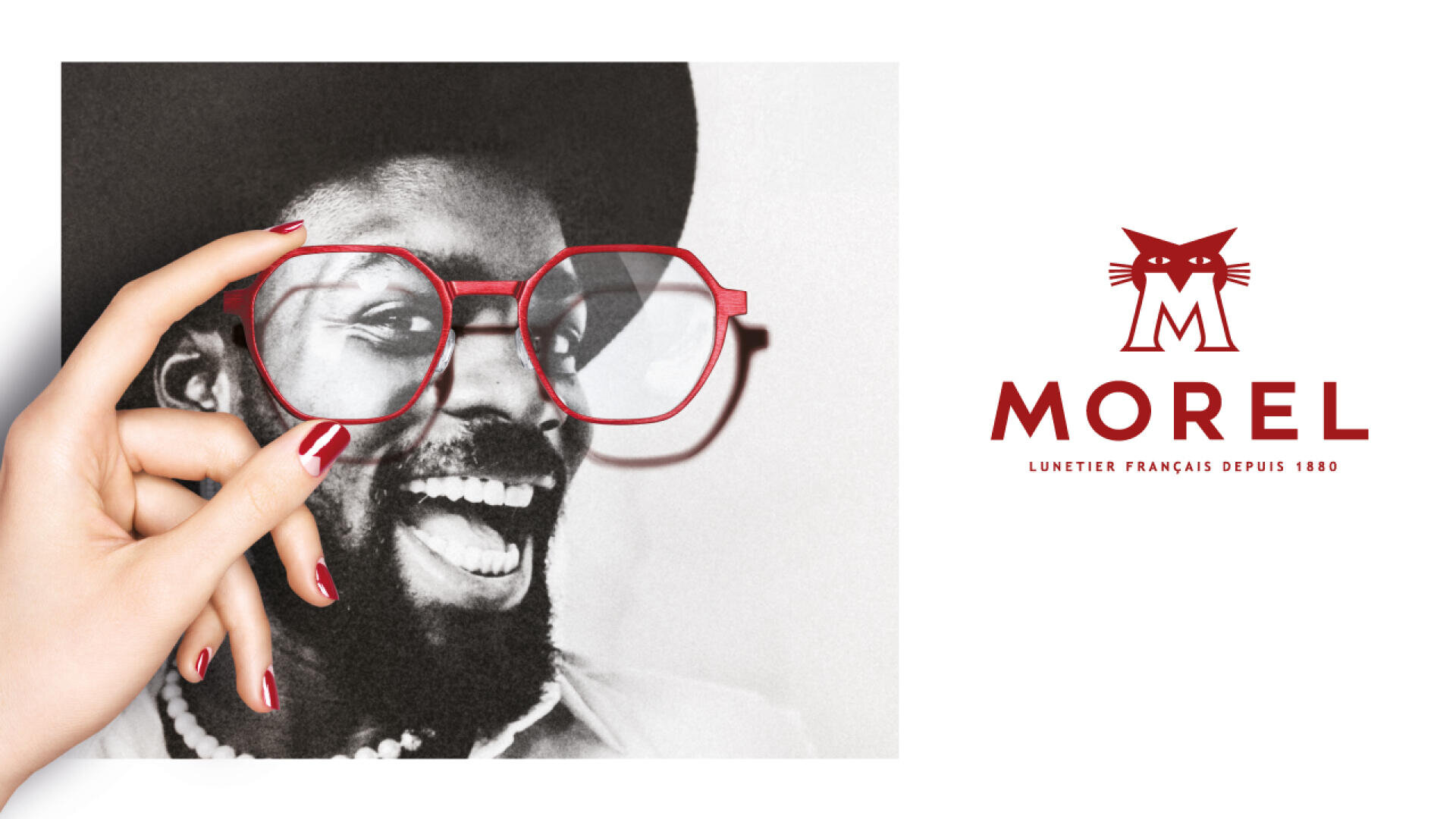 Eine Hand mit rotem Nagellack hält eine rote Brille über einem Schwarzweißfoto eines lächelnden Mannes mit Bart und Hut; rechts erscheinen das rote Logo und der Text von Morel Eyewear auf einem weißen Hintergrund.