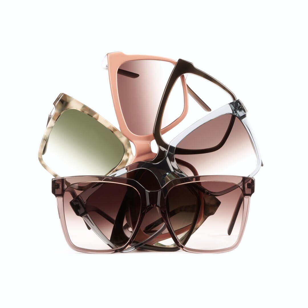 Ein stilvolles Arrangement von fünf übergroßen Sonnenbrillen in verschiedenen Farben und Mustern, darunter Rosa, Schildpatt, Weiß und Brauntöne, die vor einem weißen Hintergrund aufeinander gestapelt sind.