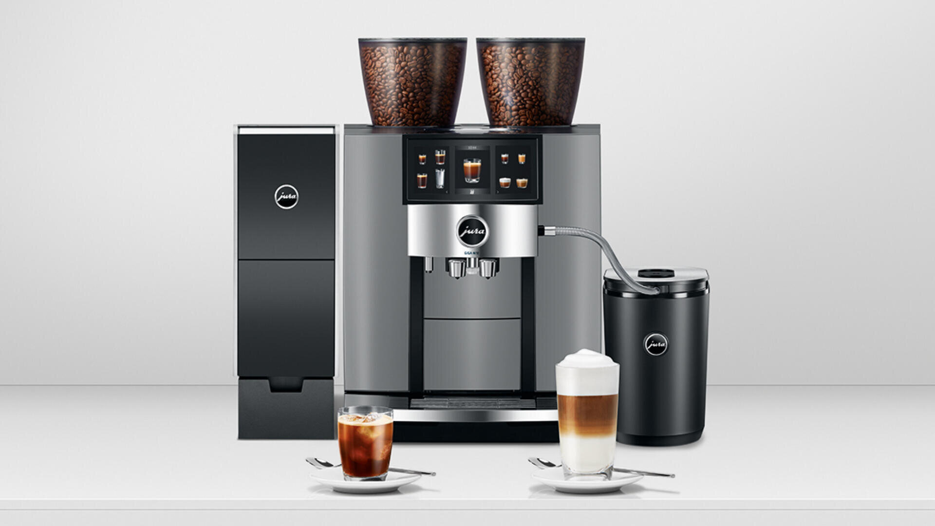 Auf einer Theke steht ein moderner Kaffeevollautomat mit zwei Bohnenbehältern, Touchscreen-Display und Milchaufschäumer, davor stehen Tassen mit Eiskaffee und geschichtetem Latte Macchiato.