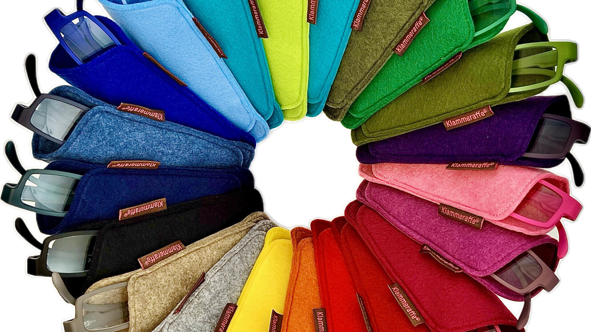 Eine kreisförmige Anordnung von Brillen in weichen, bunten Filzetuis, die ein Regenbogenmuster in den Farben Blau, Grün, Gelb, Rot, Rosa und Schwarz bilden und alle mit der Aufschrift „Klammeraffe“ versehen sind.