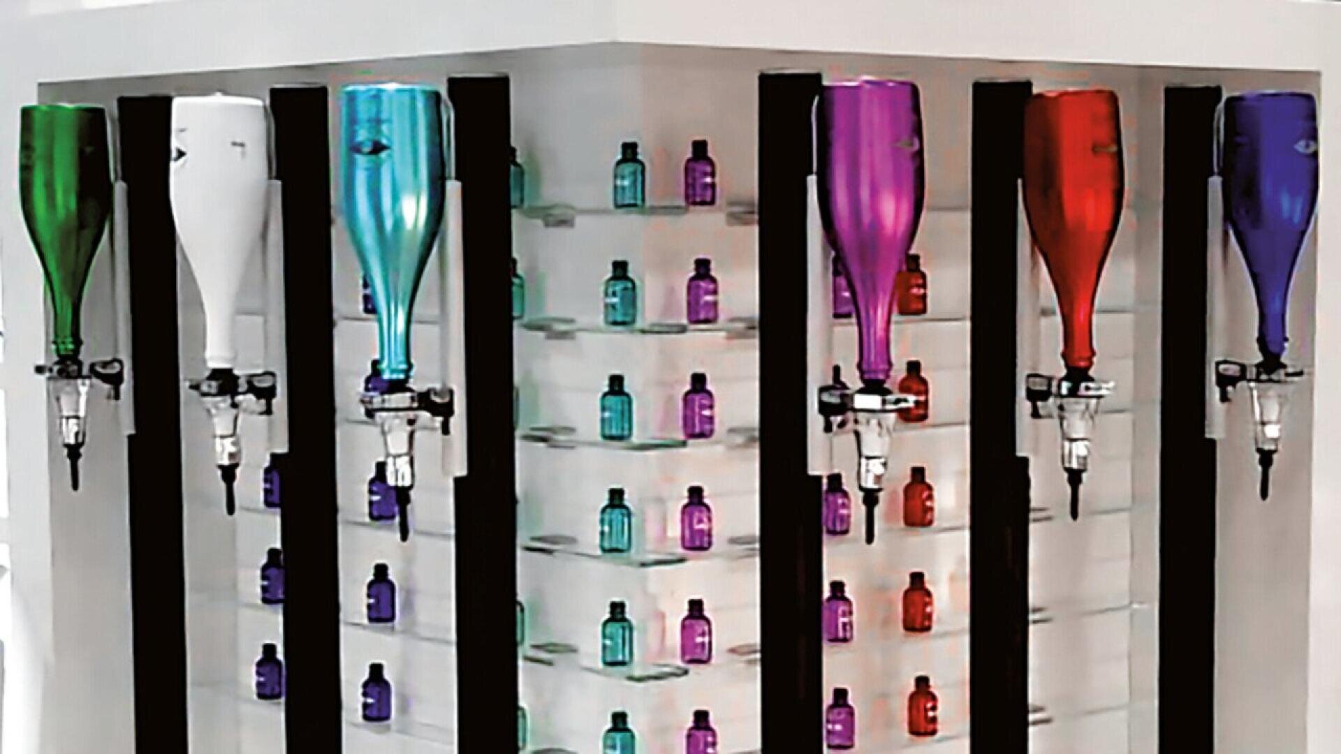 A display of large, colorful bottles mounted upside down next to rows of small, vibrant bottles on shelves. The setup appears clean and modern, likely part of a bar or beauty product display.
