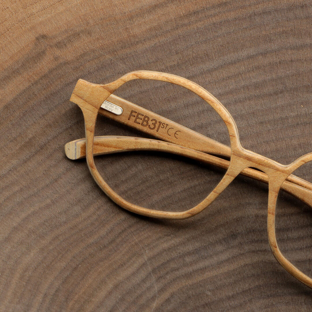 Eine runde, leichte Holzbrille ruht auf einer strukturierten Holzoberfläche. Die Innenseite des Bügels ist mit FEB 31ST graviert.
