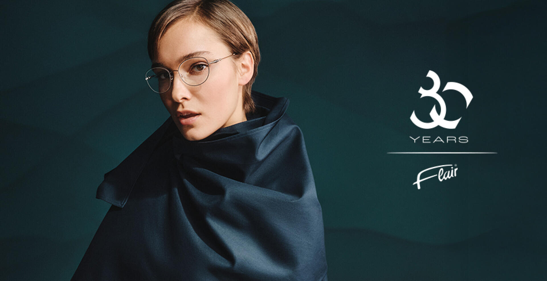 A person with round glasses and a dark, silky scarf stands in front of a dark, textured background. The text reads 30 years of flair, an anniversary.