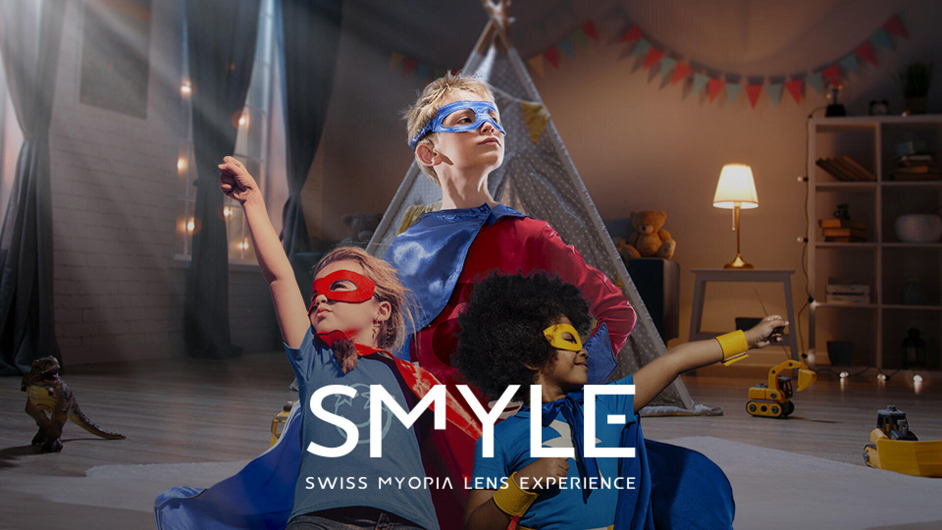 Three children in colorful superhero costumes pose confidently in a comfortably furnished living room with toys on the floor. The text SMYLE SWISS MYOPIA LENS EXPERIENCE is displayed below.