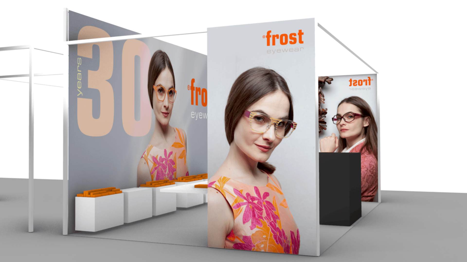 Ein Messestand von frost eyewear zeigt großformatige Bilder einer Frau, die eine elegante Brille und ein orange-rosa Blumenkleid trägt, mit modernen Sitzgelegenheiten und Displays, die Brillen präsentieren.
