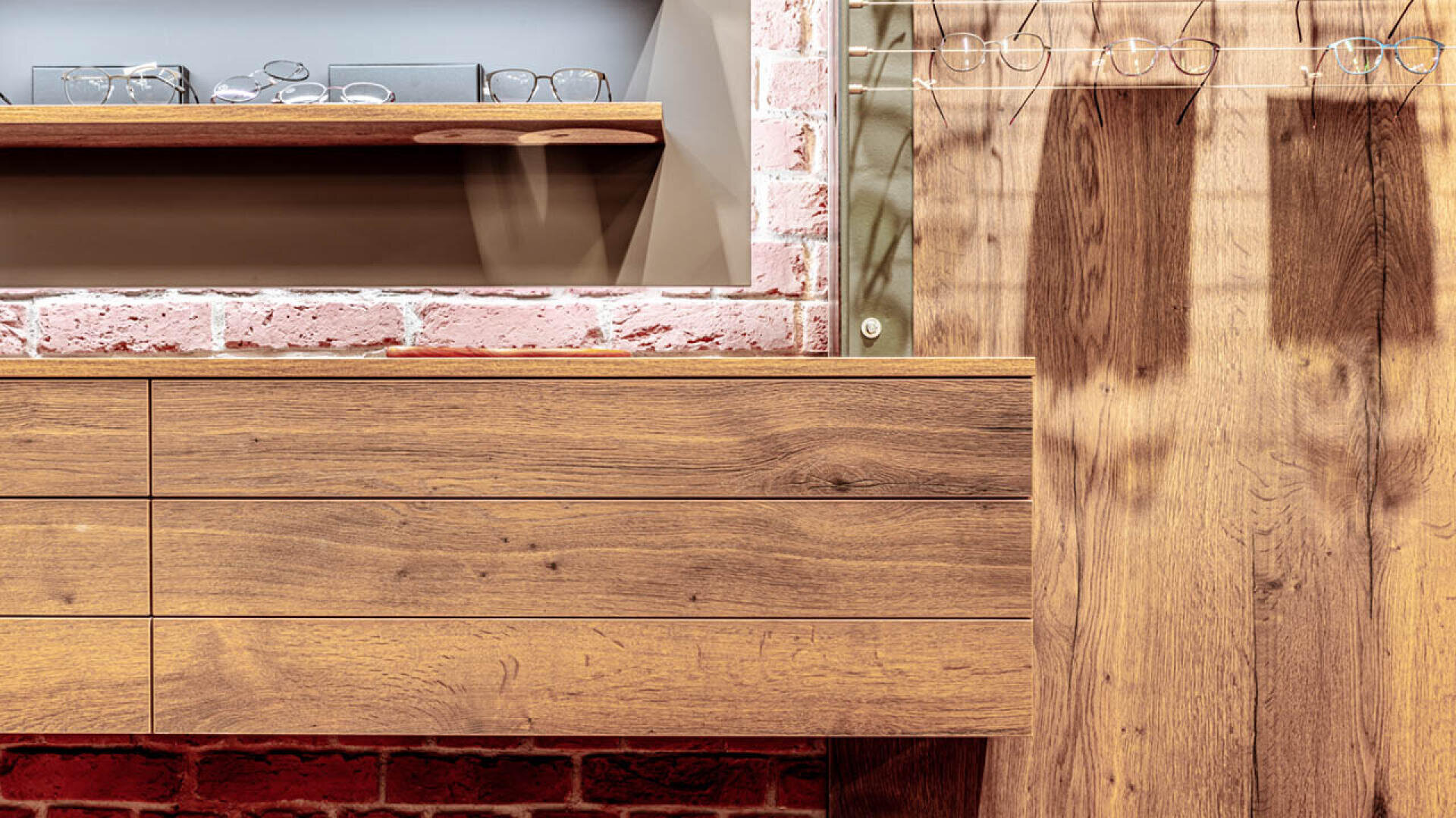 Nahaufnahme eines modernen Holzschranks und Wandregals zur Präsentation von Brillen in einem stilvollen Interieur mit Sichtmauerwerk und Holzoberflächen.