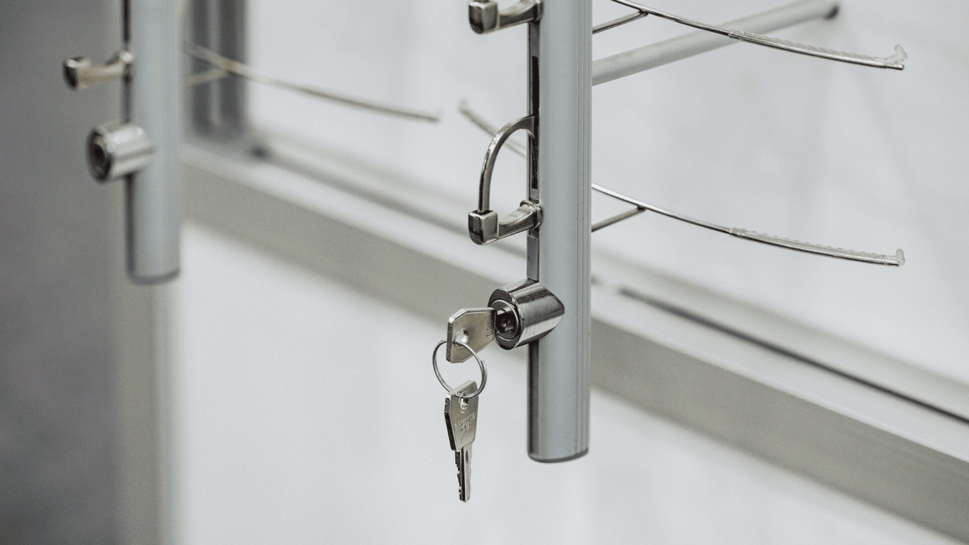 Close-up of metal lockers or storage units with a set of keys inserted into a lock on one of the units. Two metal keys are hanging from the lock by a keyring.