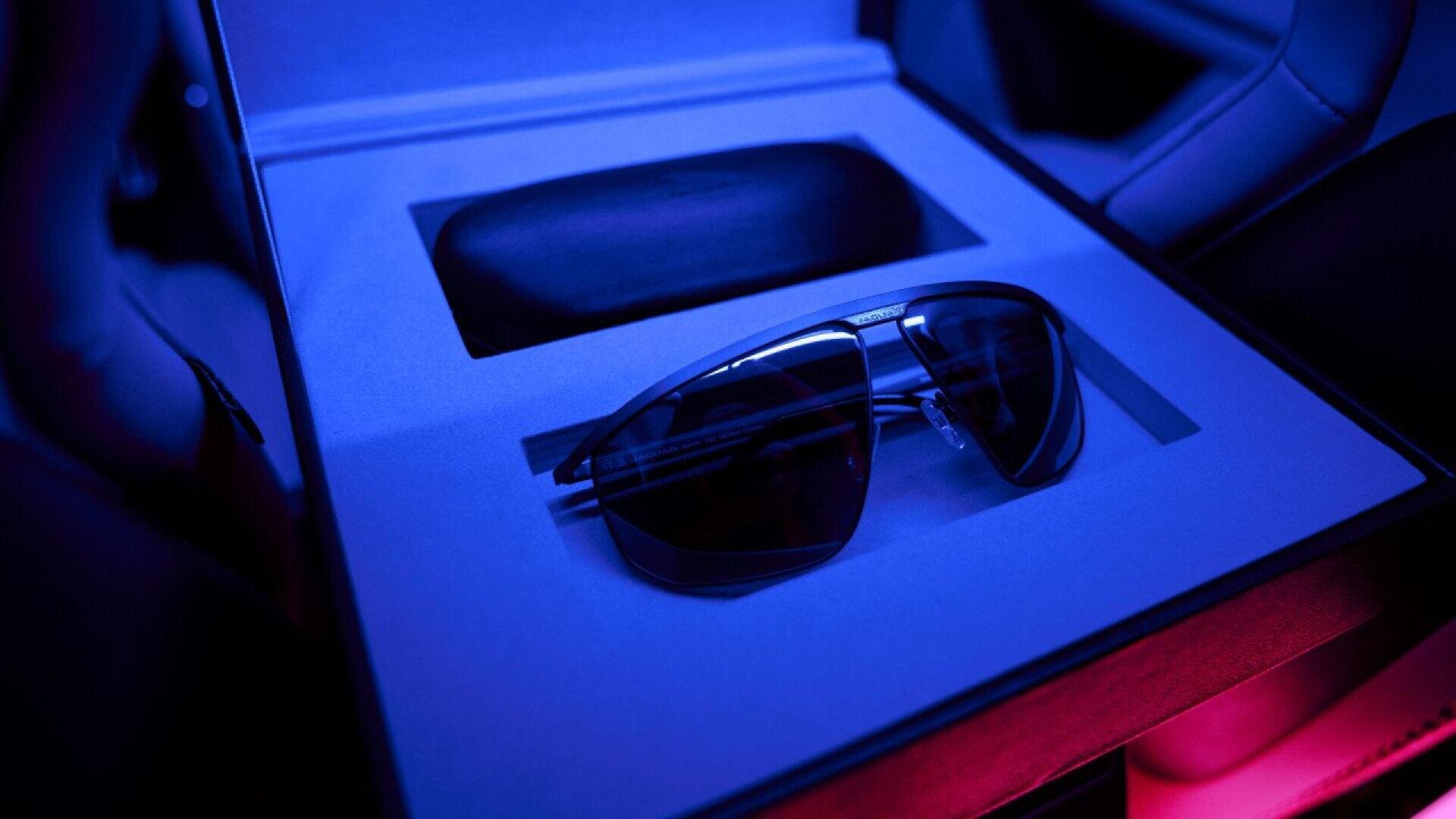 A pair of dark sunglasses sits in a fitted display box with a black case behind them, illuminated by blue and pink lighting.
