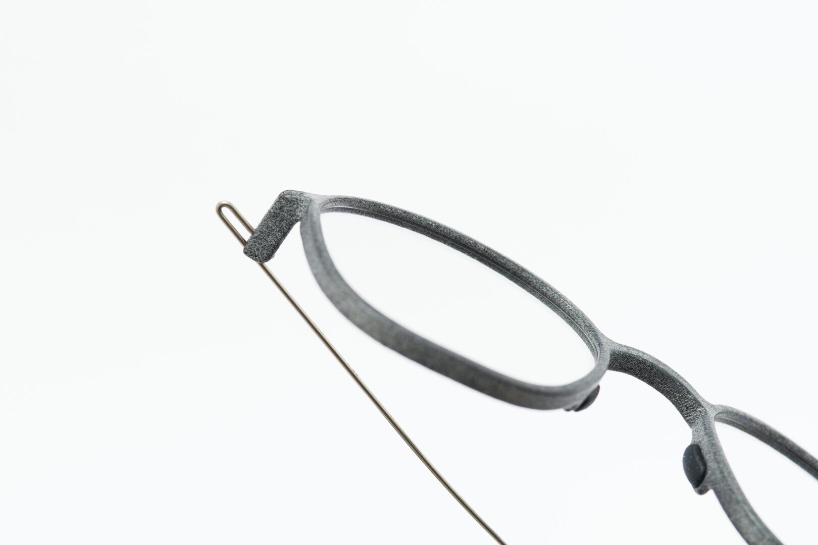 Eine Nahaufnahme der oberen Hälfte einer Brille mit grauem Rahmen und dünnem Metallbügel vor einem schlichten weißen Hintergrund.