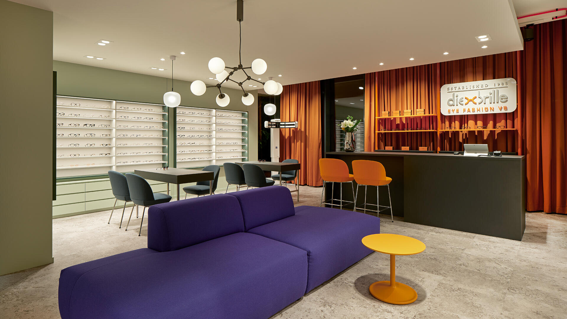 Moderne Optiker-Einrichtung mit orangefarbenen Vorhängen, einer schwarzen Theke, Brillenregalen, einem lila Sofa, einem kleinen gelben Tisch und modernen Leuchten. Der Raum ist gut beleuchtet und stilvoll gestaltet.