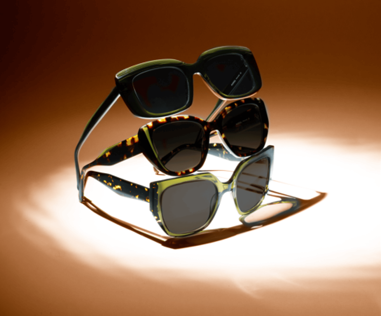 Drei Paar stilvolle Sonnenbrillen sind vertikal auf einem braunen Hintergrund gestapelt, jede mit dicken Rahmen in verschiedenen Farben und Mustern, darunter einfarbig grün, schildpatt und grün gesprenkelt.