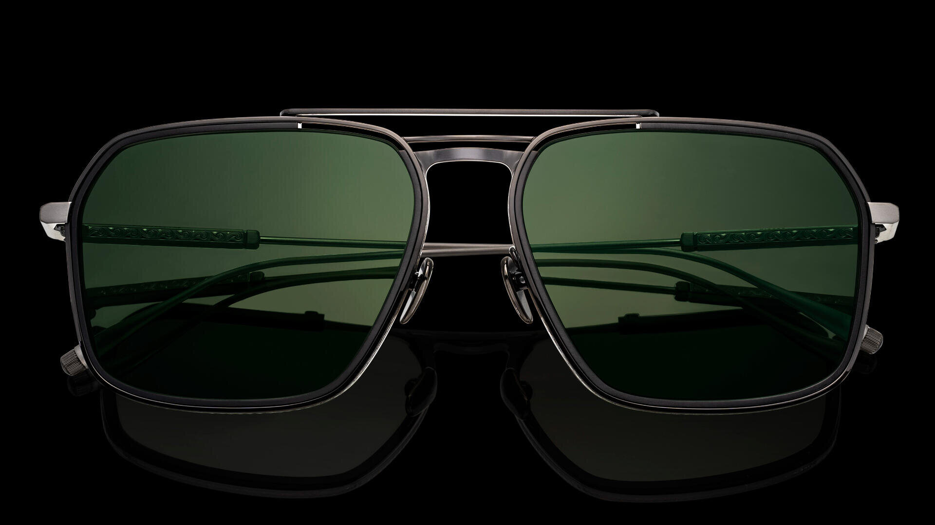 Nahaufnahme einer stylischen Pilotensonnenbrille mit schwarzem Metallrahmen und dunkelgrünen Gläsern vor schwarzem Hintergrund.