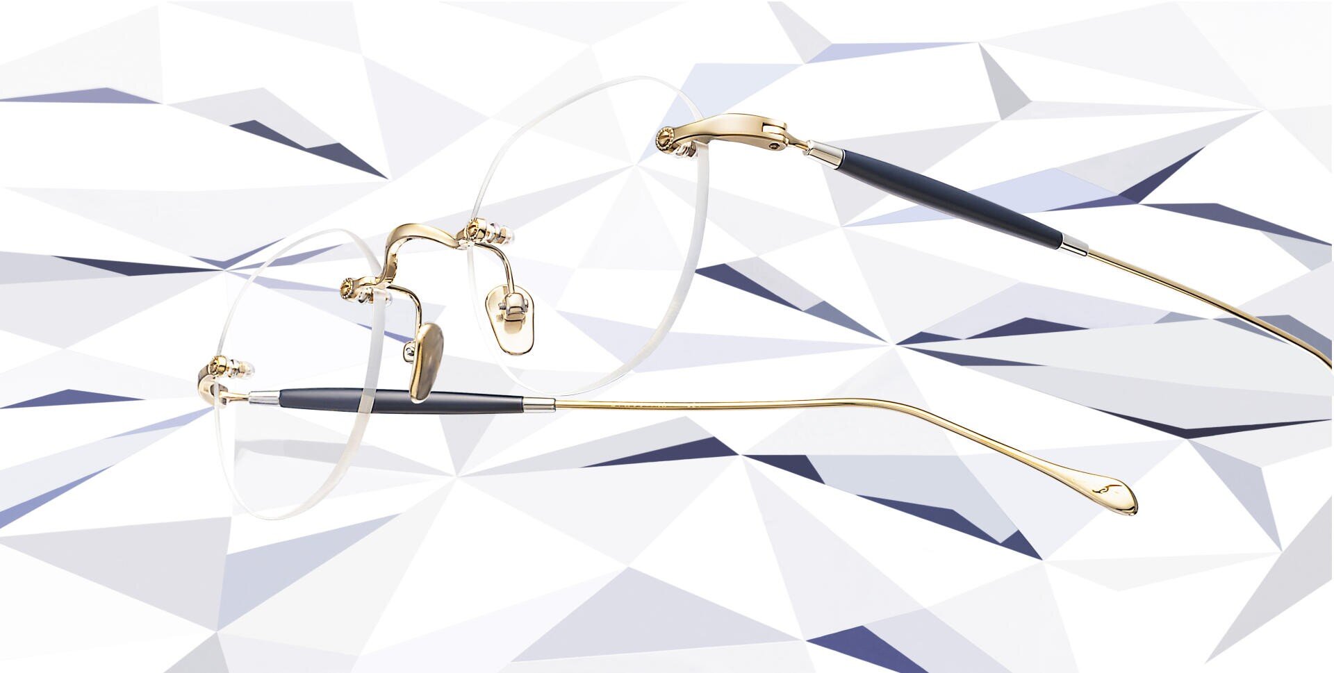 Eine randlose Brille mit goldenen Bügeln und schwarzen Akzenten, die vor einem geometrischen, facettierten Hintergrund in Weiß und Grau steht.