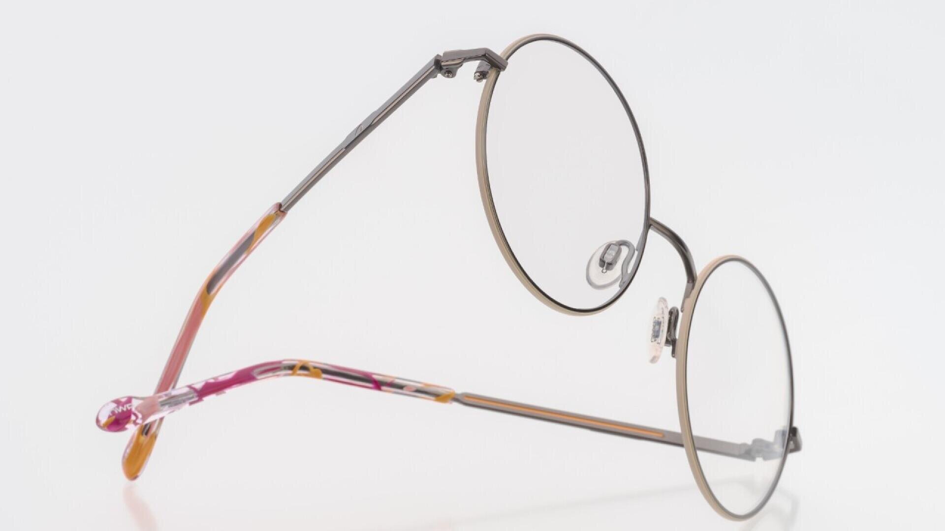 A pair of round, metal-rimmed eyeglasses with thin frames and clear lenses, featuring brown and pink-tinted temple tips, displayed on a white background.