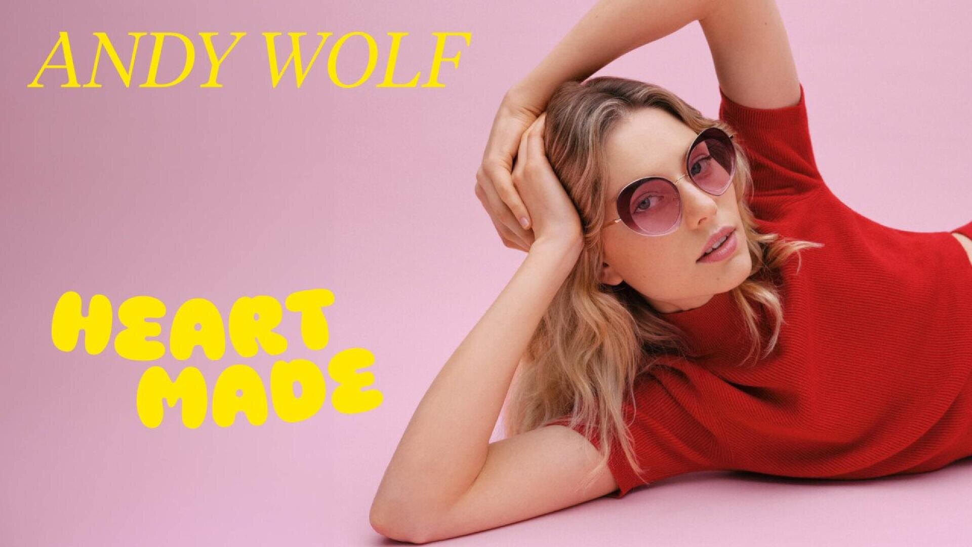 A woman in a red top reclines on a pink surface, wearing round pink sunglasses. Bold yellow text reads “ANDY WOLF” at the top left and “HEART MADE” at the bottom left.