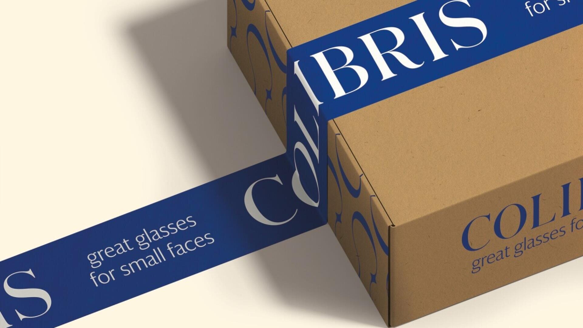 A brown cardboard box is sealed with blue tape that reads, COLIBRIS great glasses for small faces, in white text. The box is placed on a light surface.