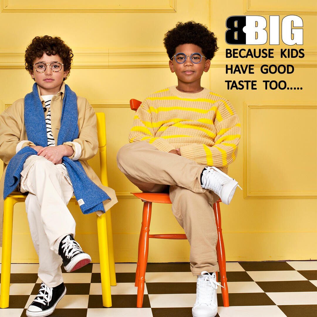 Two children with curly hair sit confidently on yellow and orange chairs against a yellow wall. Both wear glasses and stylish outfits. Text reads, BIG Because kids have good taste too.....