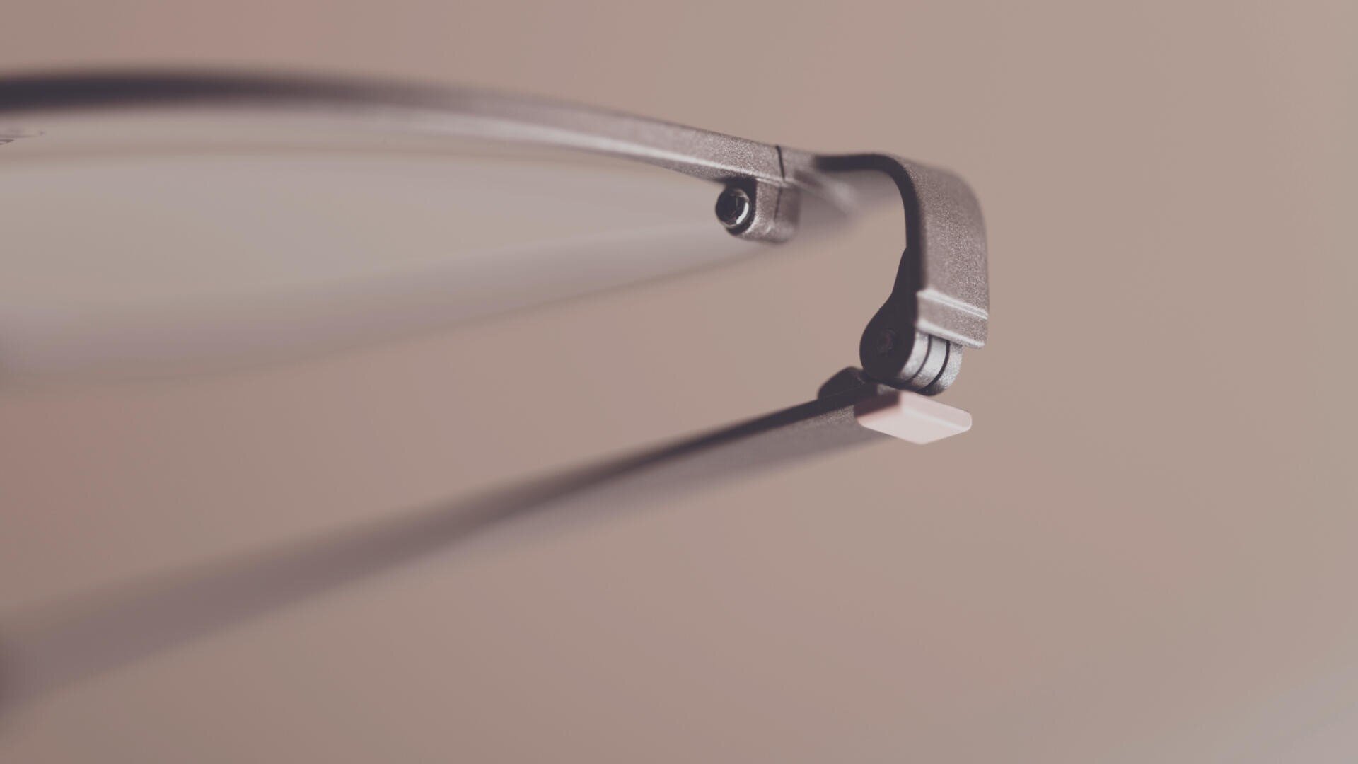Nahaufnahme des Scharniers und Bügels einer Brille mit einem sanften beigen Hintergrund und geringer Tiefenschärfe, die das metallische Scharnierdetail hervorhebt.