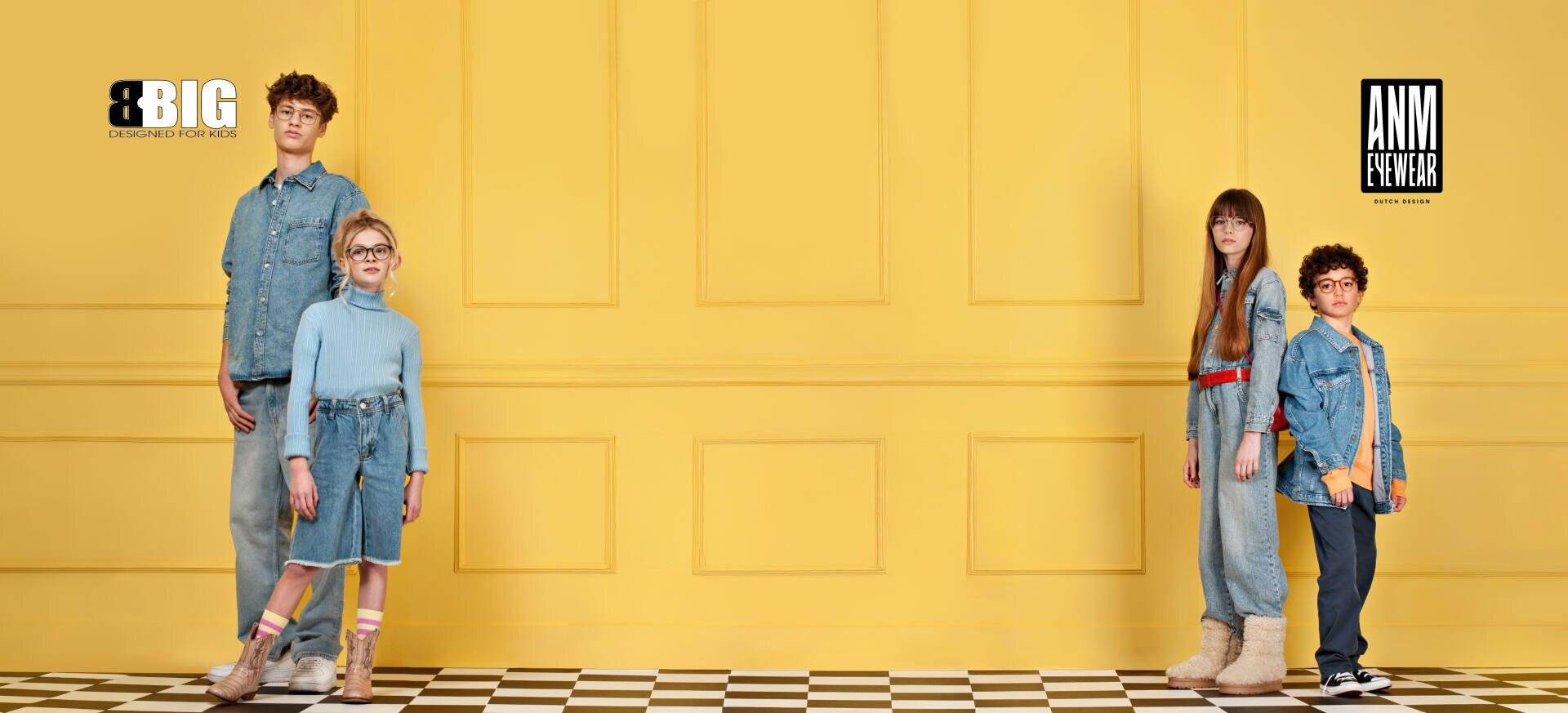 Four children stand in front of a yellow wall on a black and white checkered floor, wearing blue jeans and glasses. Two logos, BIG and ANN FOREVER, appear in the upper corners of the picture.