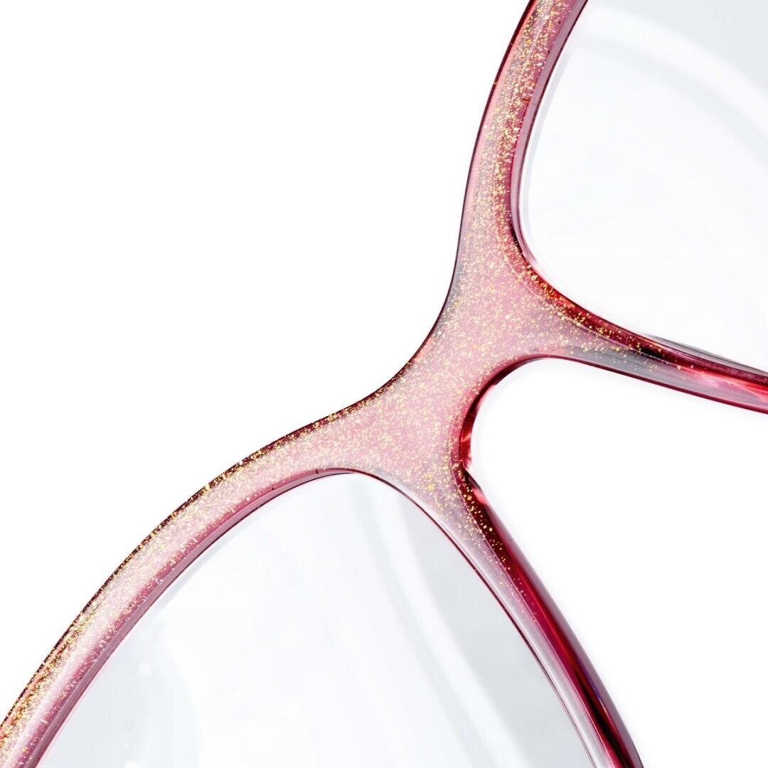 Nahaufnahme einer Brille mit durchscheinendem rosafarbenem Gestell und dezentem Glitzer, die einen Teil des Stegs und zwei Glasränder vor einem weißen Hintergrund zeigt.