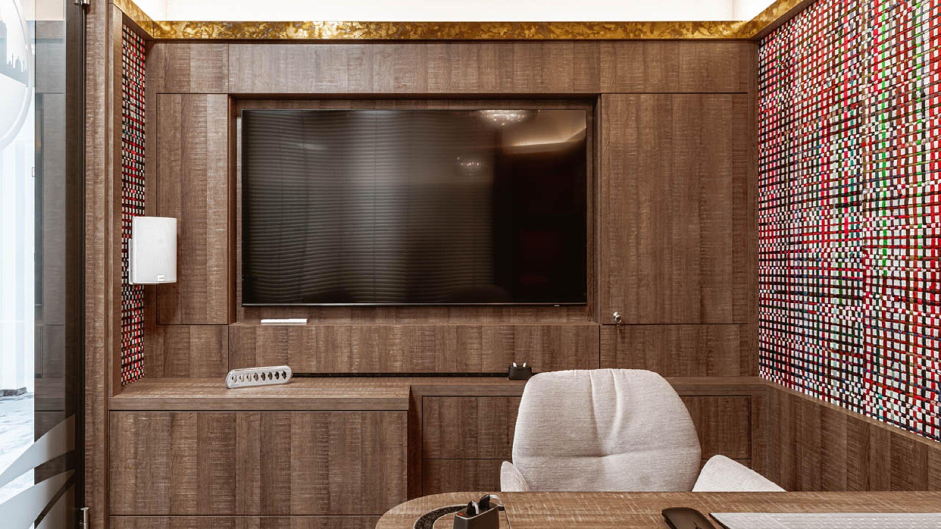 Ein modernes Büro mit Holzvertäfelung, einem großen Flachbildfernseher an der Wand, einem beigen Bürostuhl, einem Holzschreibtisch und Wänden mit einem roten, weißen und schwarzen geometrischen Muster.