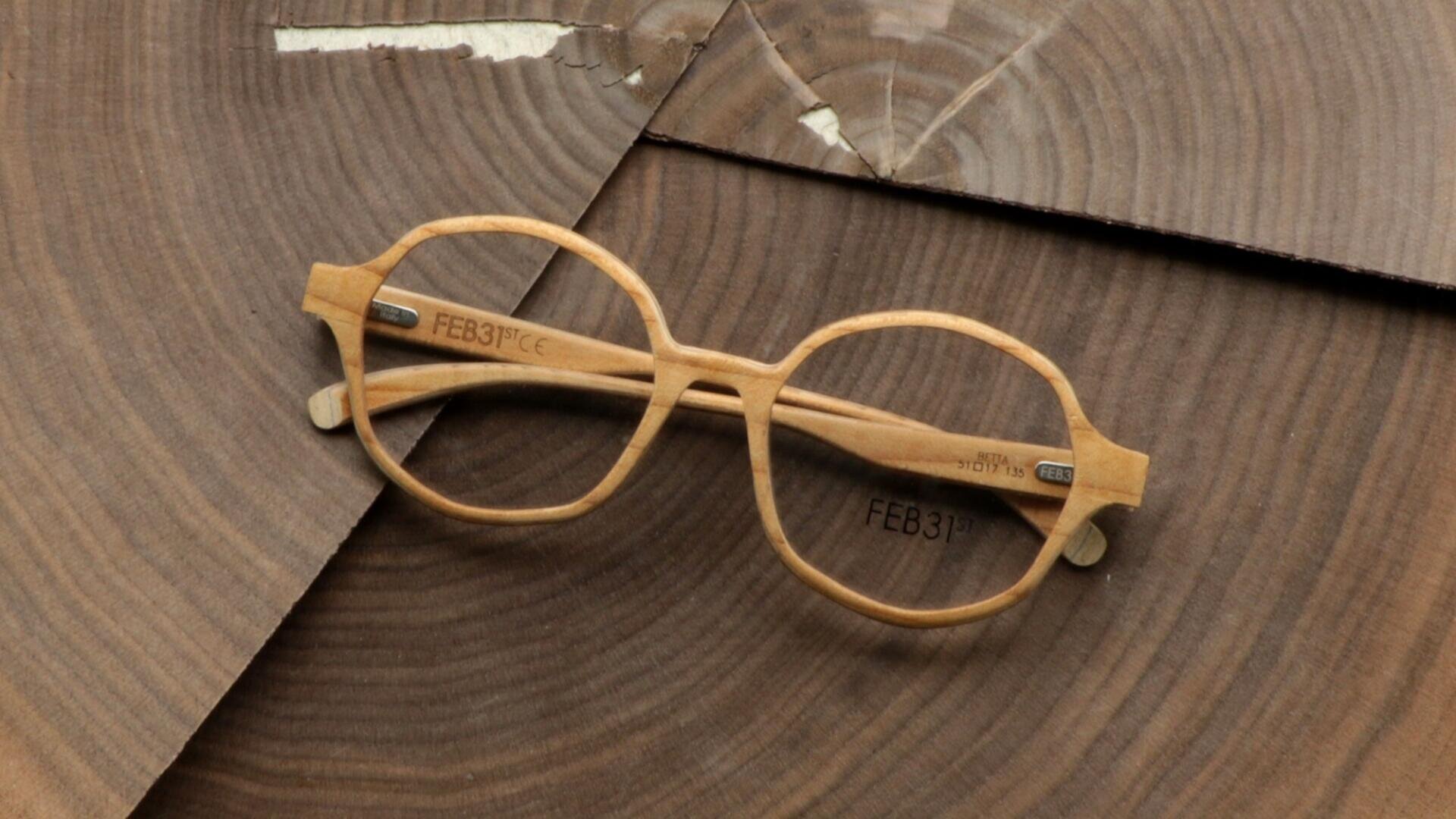 Runde, helle Holzbrille mit eingraviertem FEB31st auf den Bügeln, die auf sich überlappenden Holzstücken mit sichtbaren Jahresringen und natürlichen Strukturen ruhen.