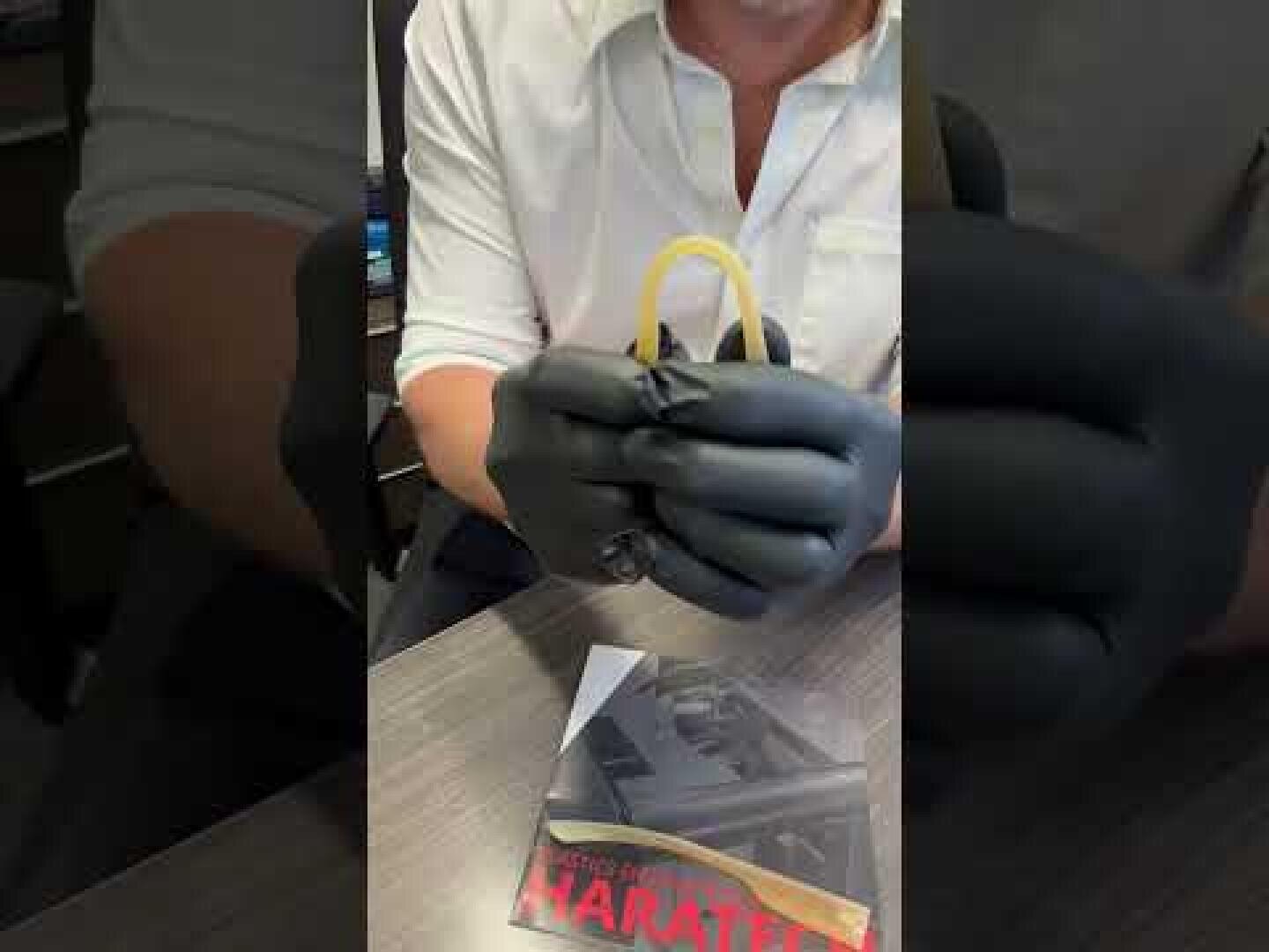 Eine Person mit weißem Hemd und schwarzen Handschuhen hält einen gelben Kofferdam in der Hand. Auf dem Schreibtisch vor ihnen liegt eine Broschüre mit dem Titel MARALEE.