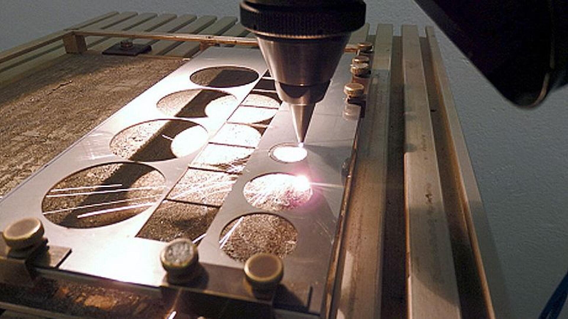 Eine Laserschneidmaschine schneidet präzise kreisförmige Formen in ein Metallblech, wobei der Laserstrahl helle Funken und Licht auf der Oberfläche erzeugt.