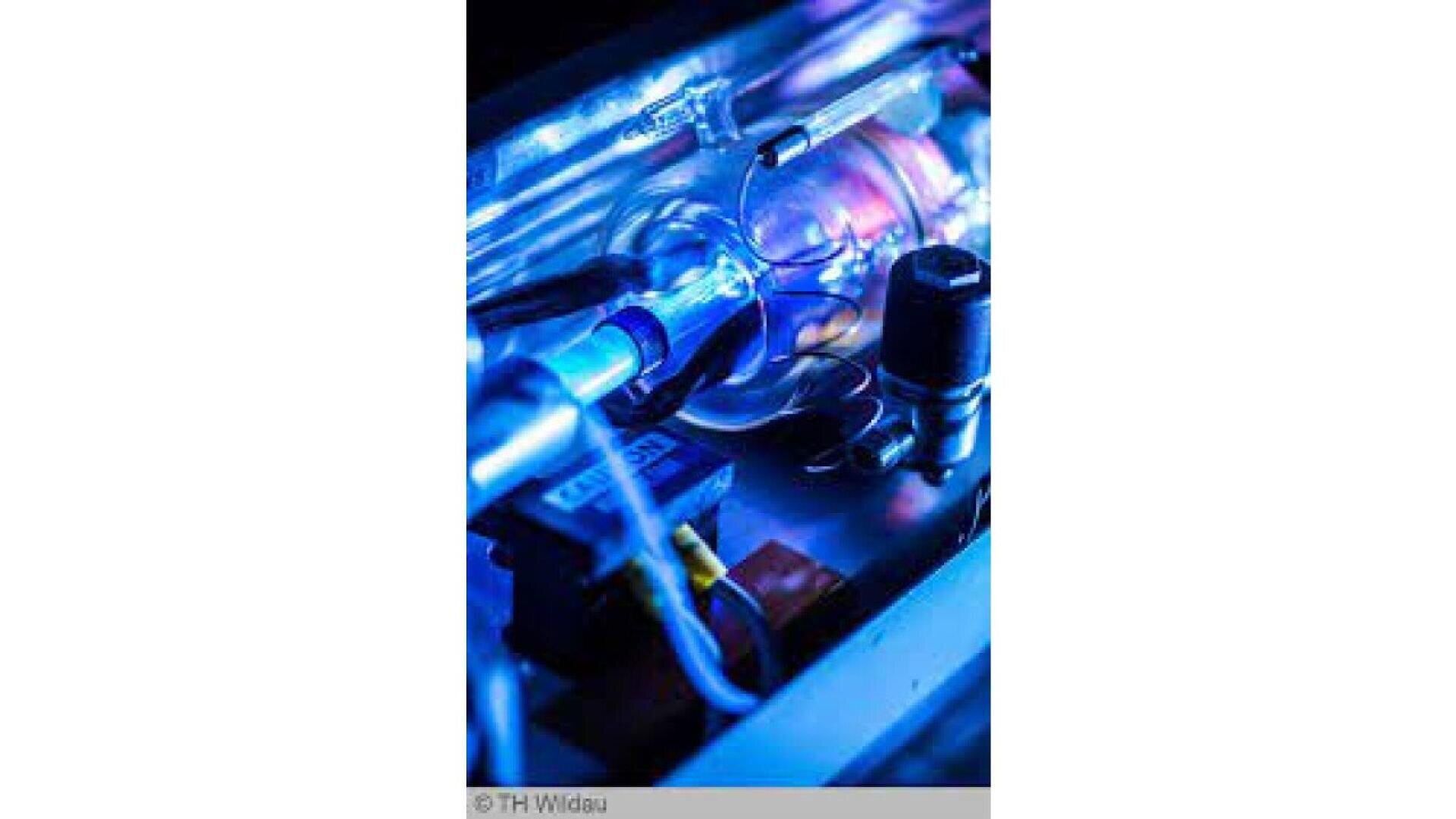A close-up view of electronic components and wiring inside scientific equipment, illuminated by blue and purple lights, showing tubes, connectors, and cables.