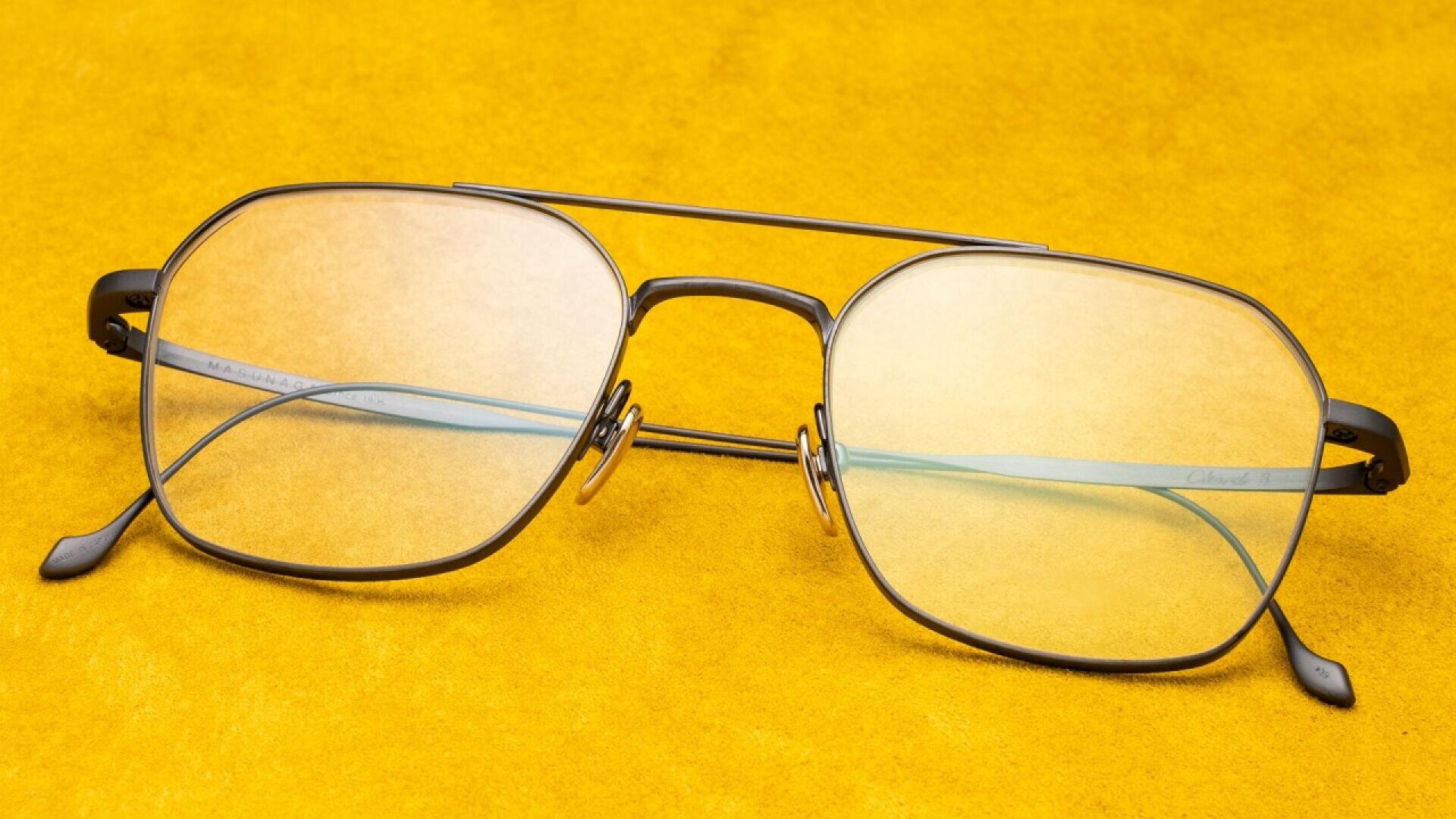 A pair of black-rimmed aviator-style eyeglasses with yellow-tinted lenses resting on a bright yellow surface.