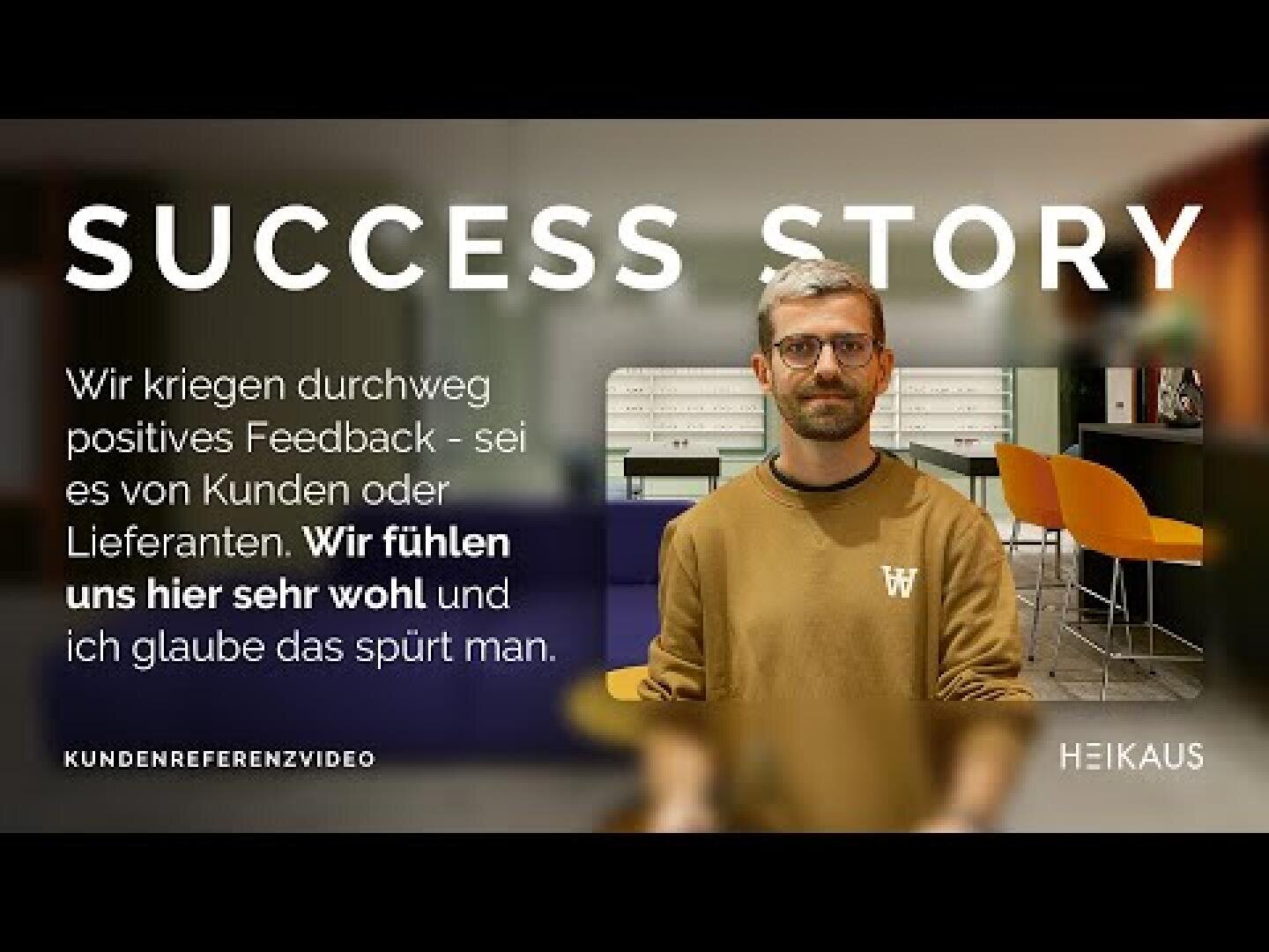 Ein Mann mit Brille und Bart steht in einem Haus und lächelt leicht. Der weiße Text über dem Bild lautet: ERFOLGSGESCHICHTE, mit einem Zitat auf Deutsch über positives Feedback und Wohlbefinden. Im Hintergrund stehen moderne Stühle und Pflanzen.