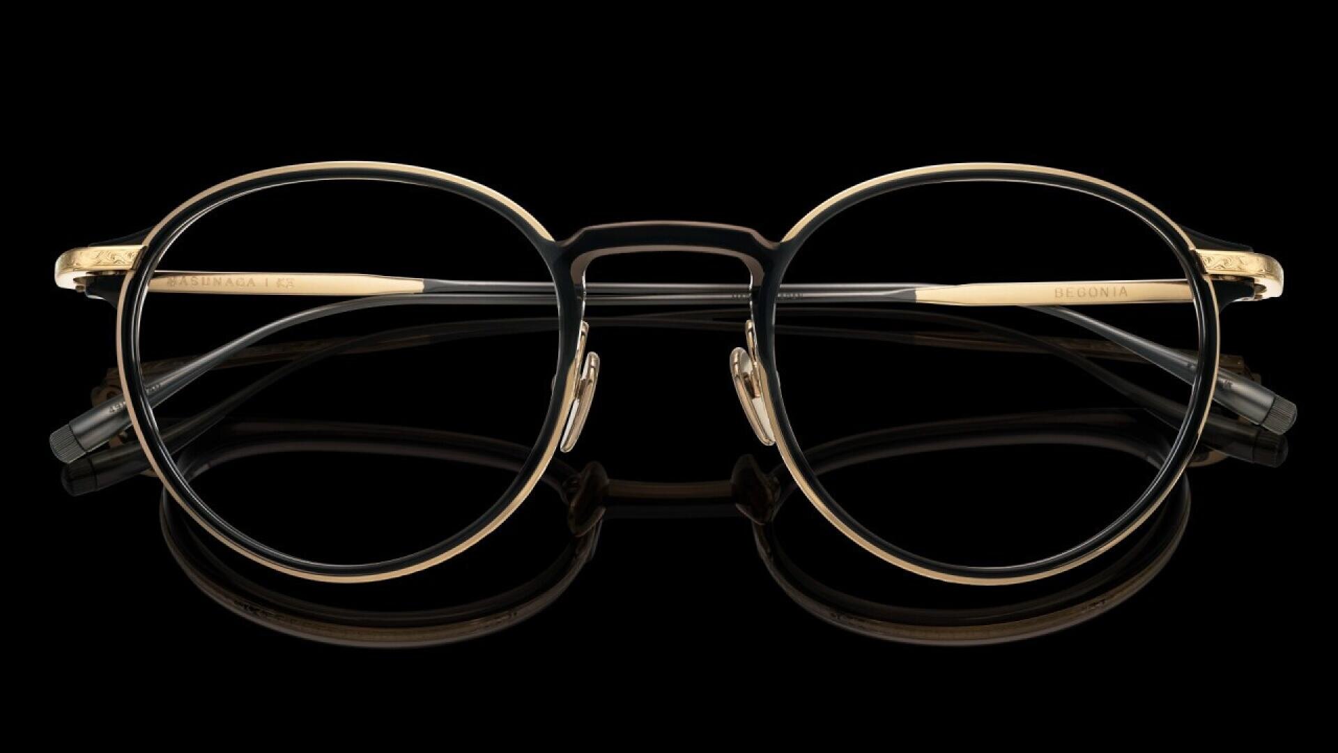 A pair of gold and black round eyeglasses with a double bridge design, displayed against a black background.
