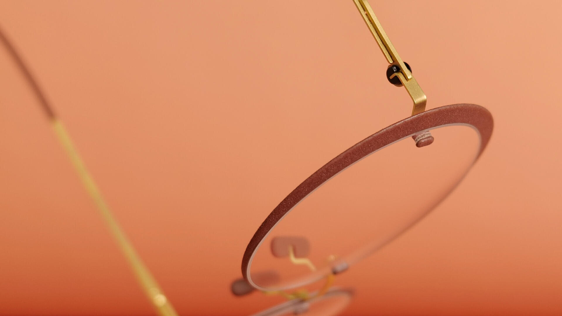 Nahaufnahme einer stilvollen Brille mit dünnem Goldrahmen und runden Gläsern vor einem sanften orangefarbenen Hintergrund.