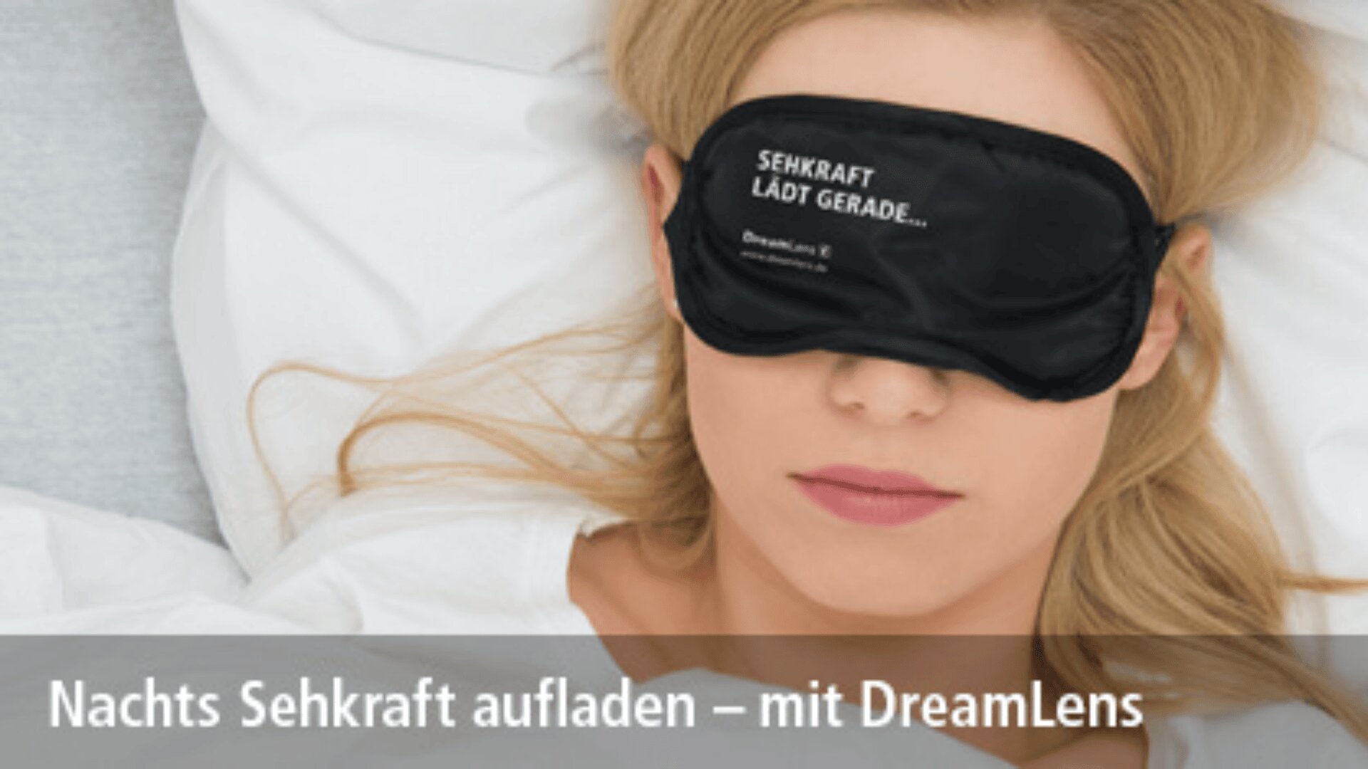 Eine Frau liegt im Bett und trägt eine schwarze Schlafmaske mit der Aufschrift "Sehkraft lädt gerade...". Unten steht: "Nachts Sehkraft aufladen - mit DreamLens.".