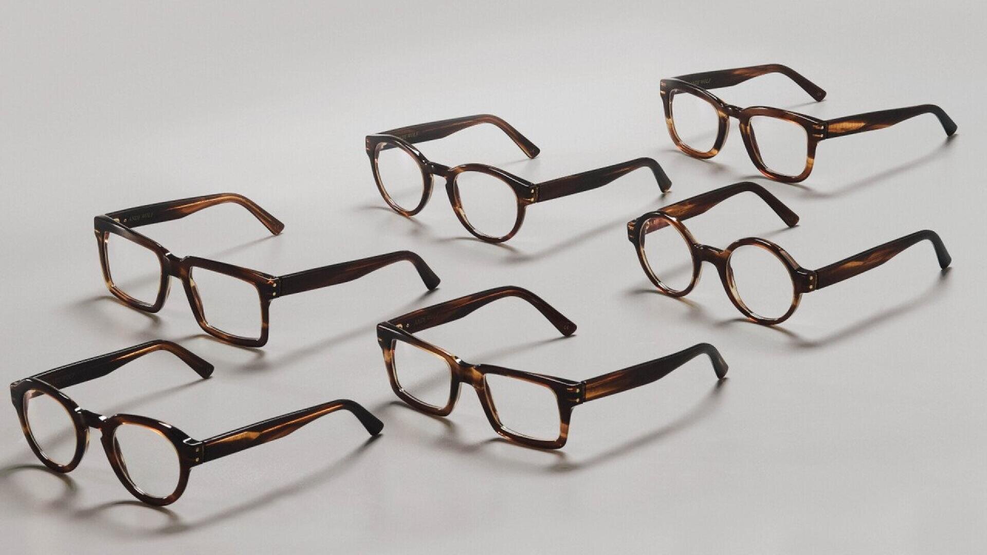 Seven pairs of brown tortoiseshell eyeglasses with clear lenses are arranged neatly on a light gray surface, with each pair facing different directions.
