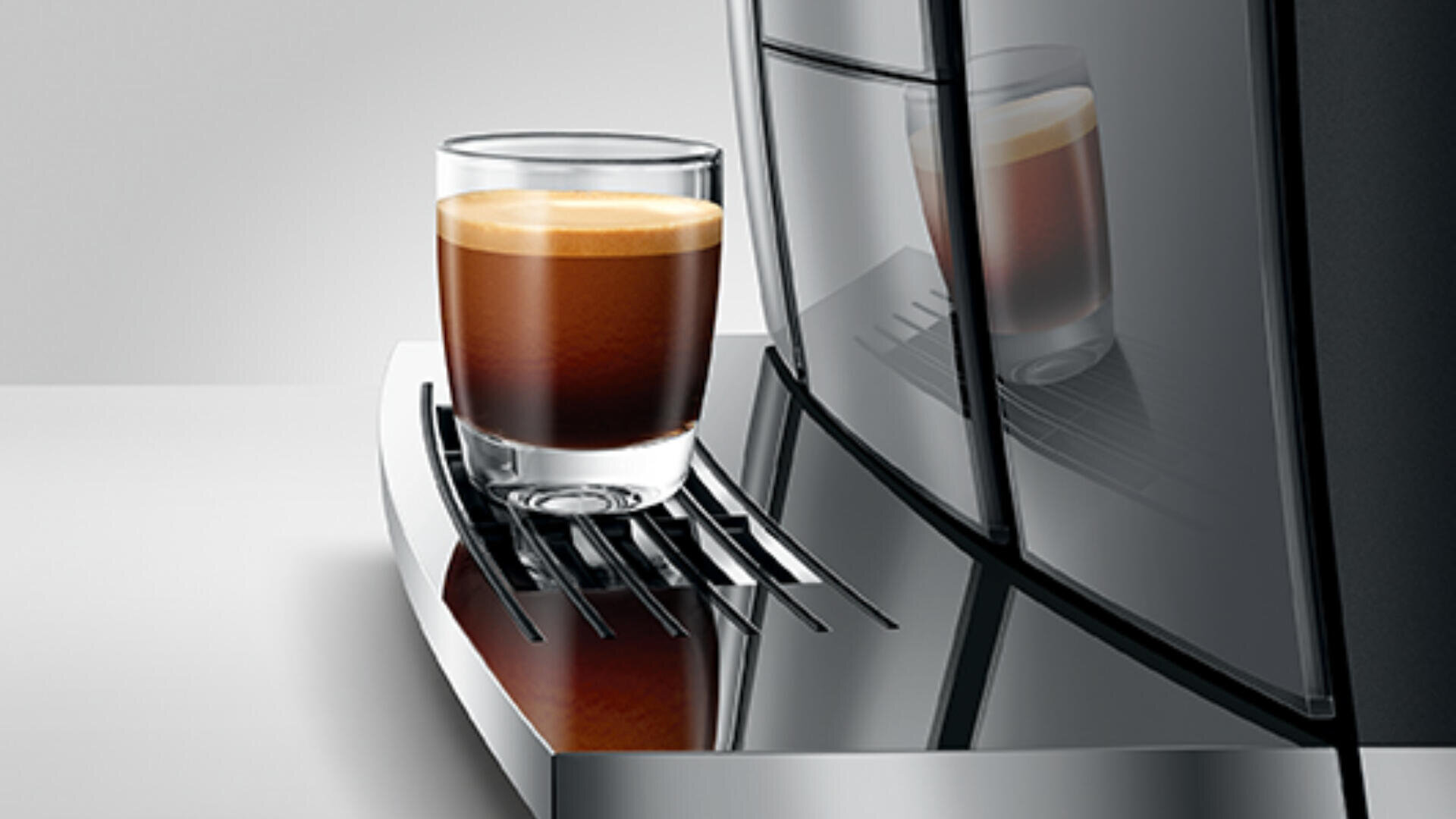 Eine mit Espresso gefüllte Glastasse steht auf der Abtropfschale eines modernen, eleganten Kaffeevollautomaten mit reflektierender Oberfläche.