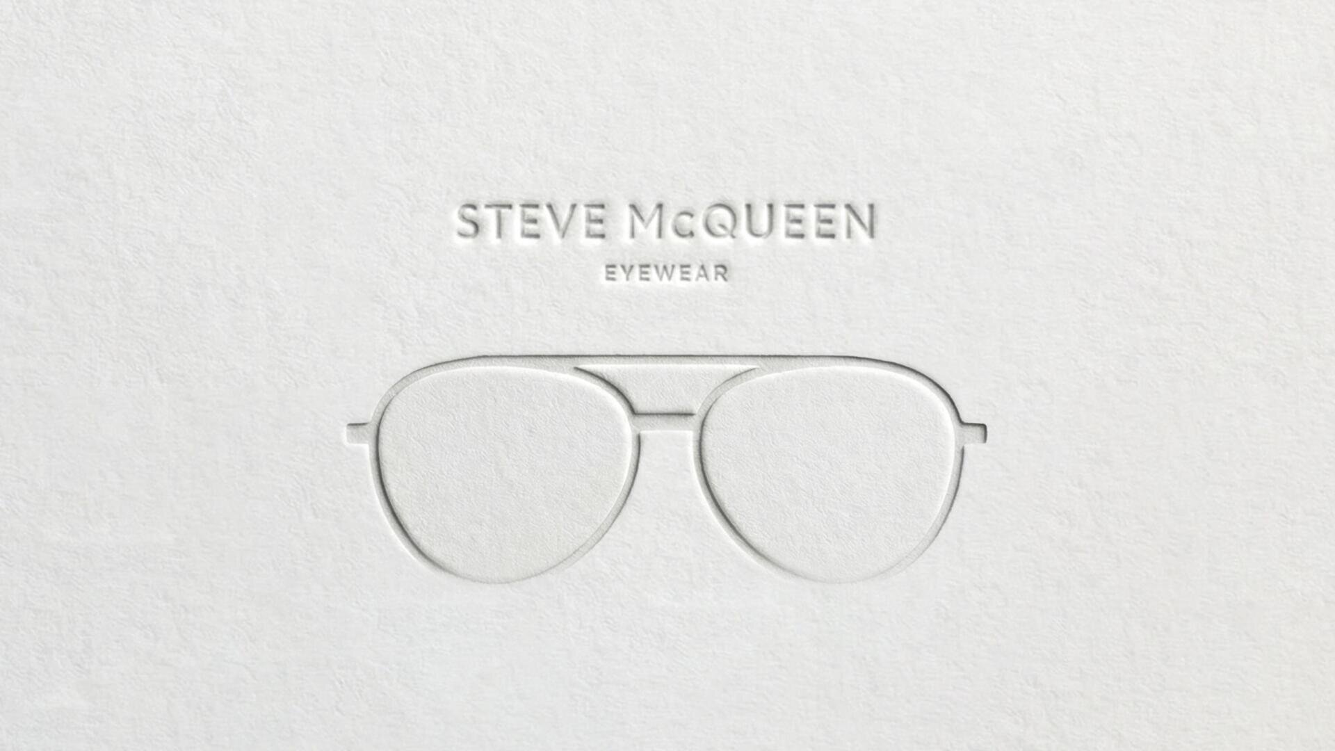 Embossed white paper features aviator eyeglasses and the text STEVE McQUEEN EYEWEAR above the glasses in raised letters. The design is minimalist and monochromatic.