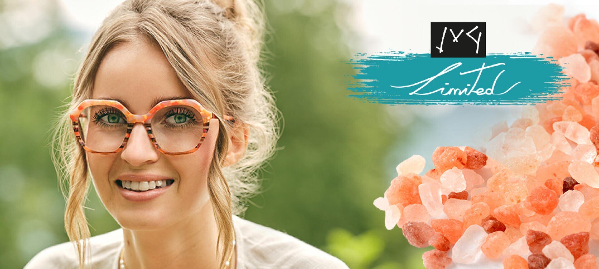 Eine lächelnde Frau mit einer großen rosa-orangen Brille ist im Freien zu sehen. Neben ihr sind rosa-weiße Salzkristalle und eine blaugrüne Grafik mit weißem Text „Limited“ aufgemalt.