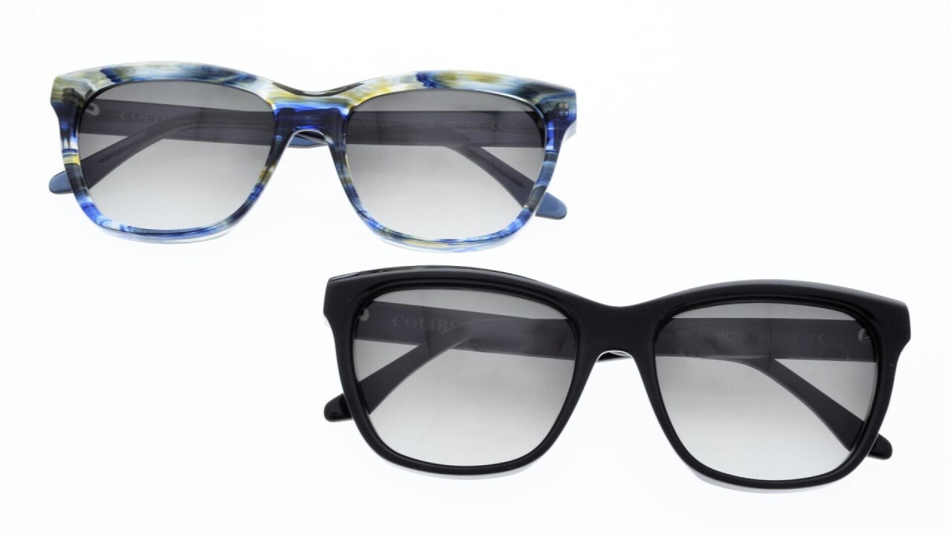 Two pairs of sunglasses with dark lenses; one pair has a black frame, and the other has a blue and beige marbled frame. Both are set against a plain white background.