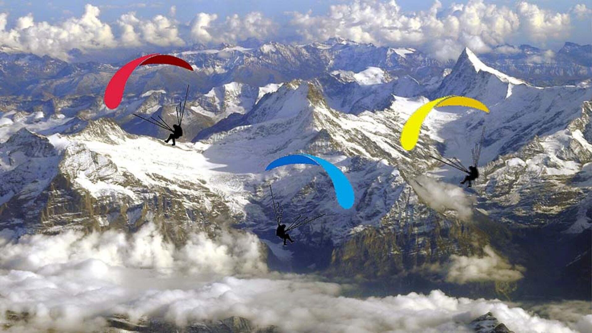 Drei Gleitschirme mit roten, blauen und gelben Schirmen schweben an einem klaren Tag über schneebedeckten Berggipfeln und Wolken.