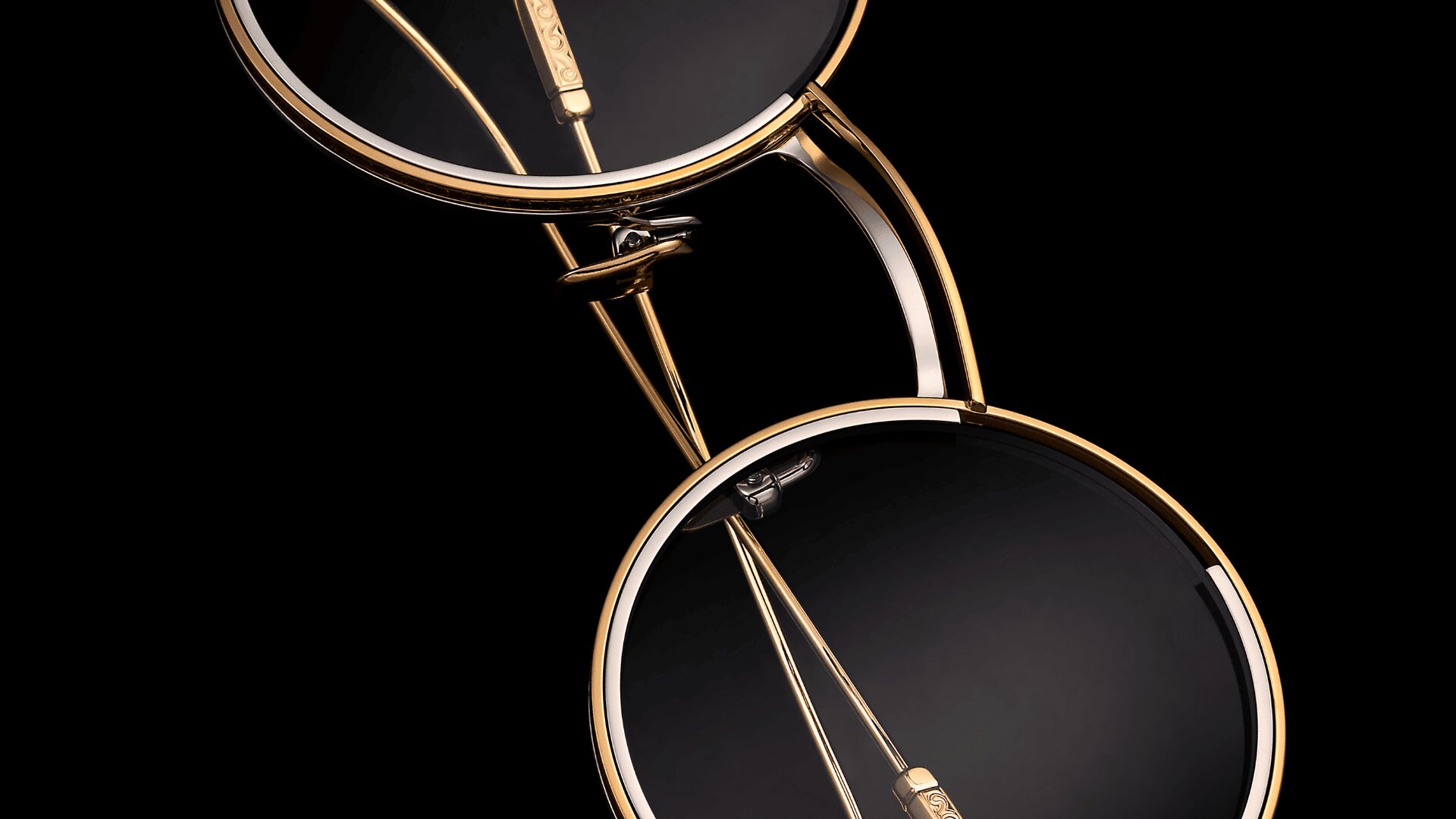 Nahaufnahme von zwei runden Brillen mit goldenen Rahmen und dunklen Gläsern, die diagonal vor einem schwarzen Hintergrund positioniert sind, was ihr elegantes und minimalistisches Design hervorhebt.