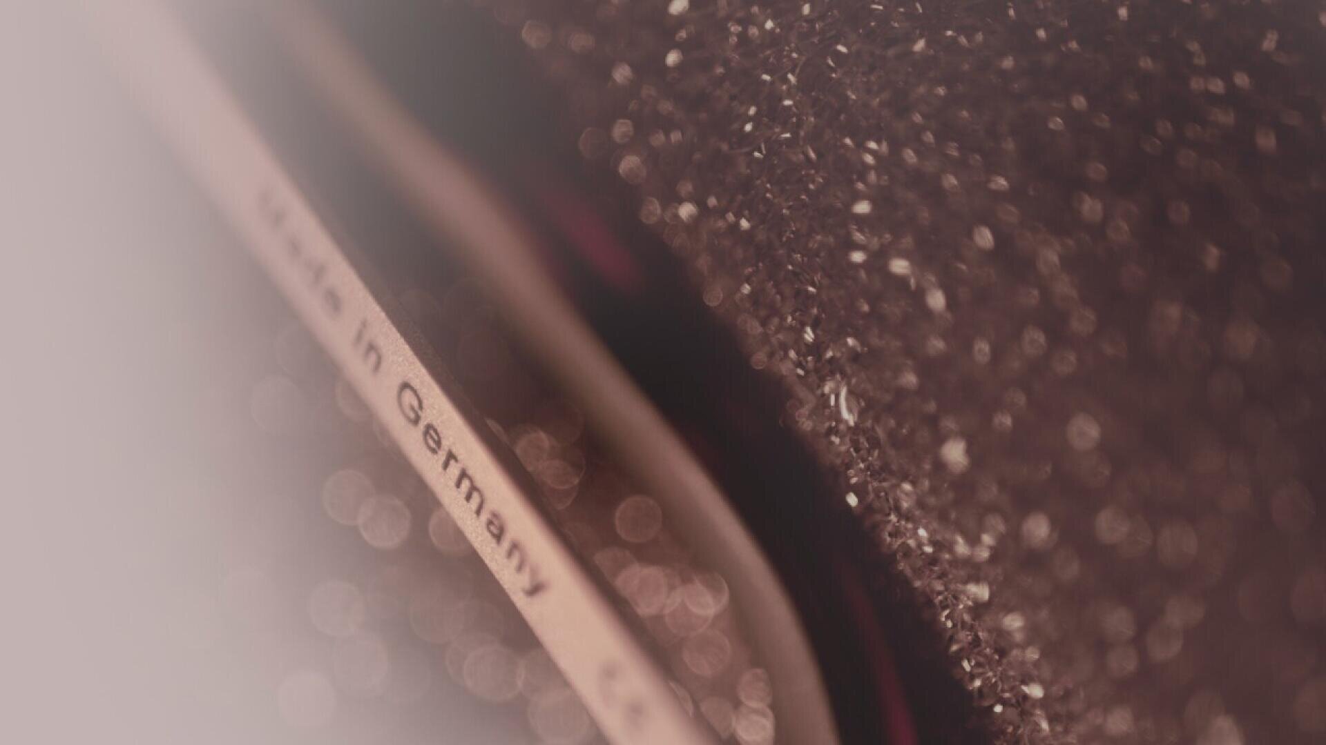 Close-up of a metallic object with the words Made in Germany partially visible, surrounded by a textured, glittery brown surface and soft out-of-focus background.