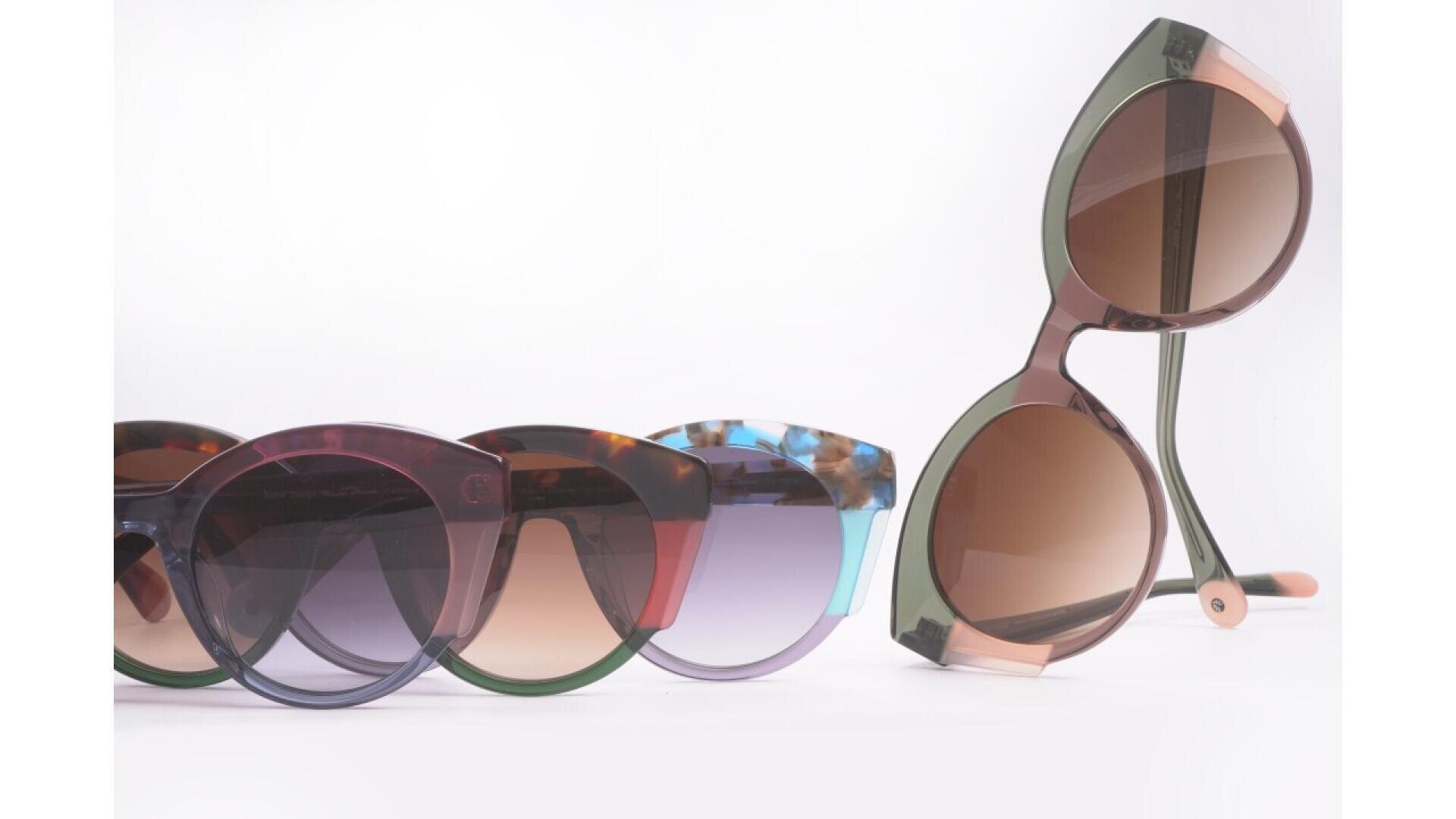 Five pairs of stylish sunglasses in various colors and designs are displayed against a white background, with one pair standing upright and the others laid out side by side in front.