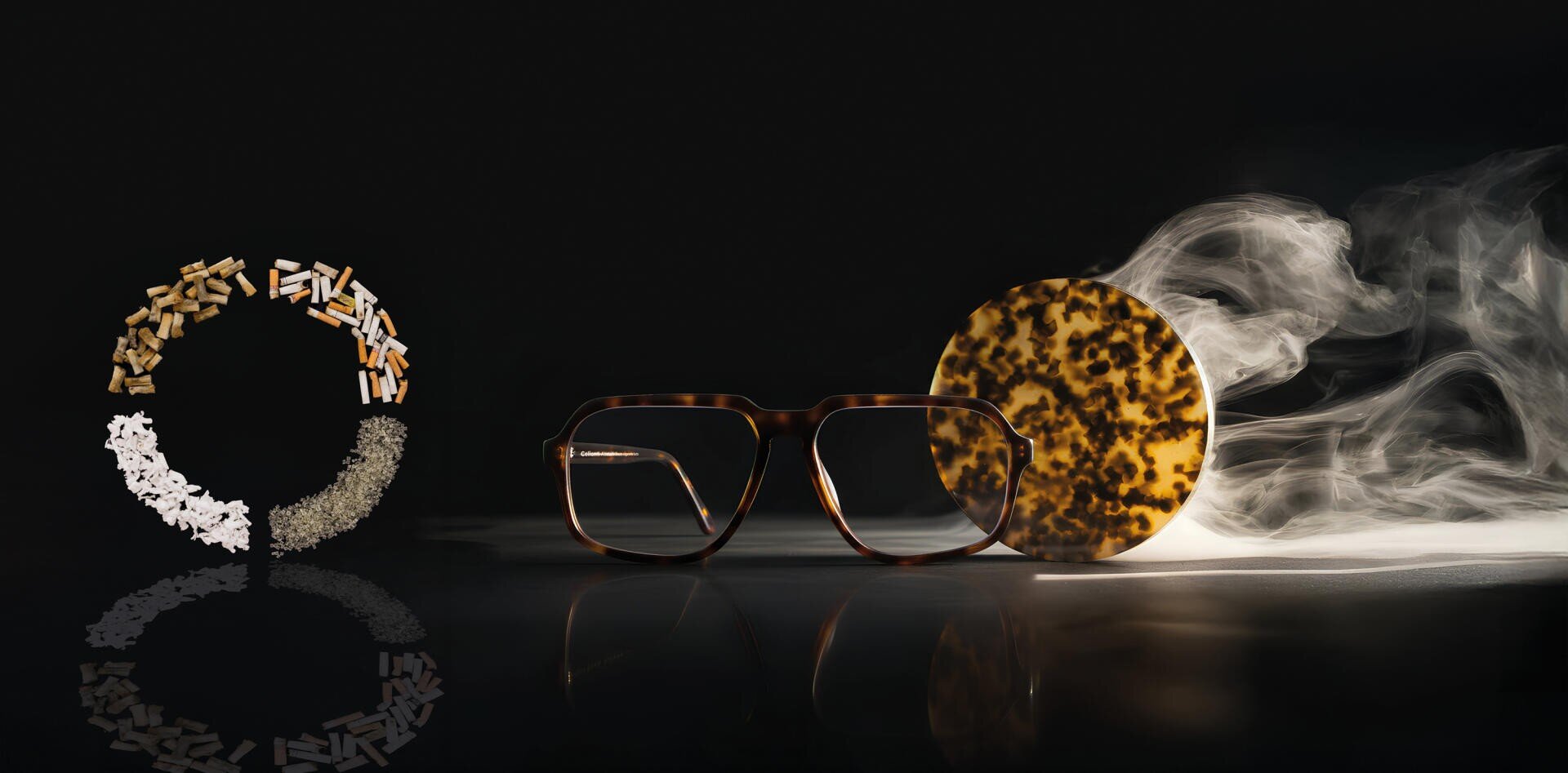 Eine Schildpattbrille sitzt zwischen einer kreisförmigen Anordnung von Zigarettenstummeln und Asche auf der linken Seite und einer runden, schildpattgemusterten Scheibe, die Rauch ausstößt, auf der rechten Seite, alles vor einem schwarzen Hintergrund.