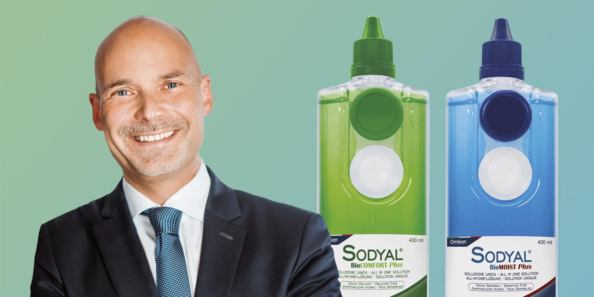 Ein lächelnder, kahlköpfiger Mann im Anzug steht neben zwei großen Flaschen mit der Aufschrift „Sodyal“, eine grün und eine blau, mit einem Hintergrund in Grün und Blau mit Farbverlauf.